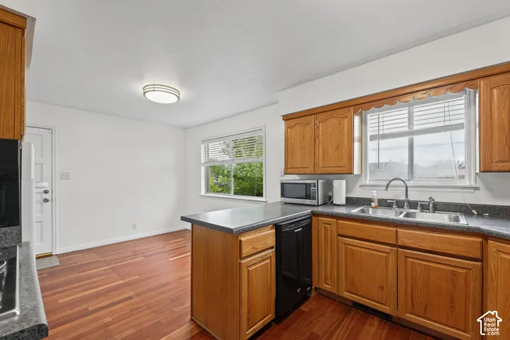 Wood-finish flooring, wood cabinetry, dark countertops, a double basin sink, and a built-in dishwasher