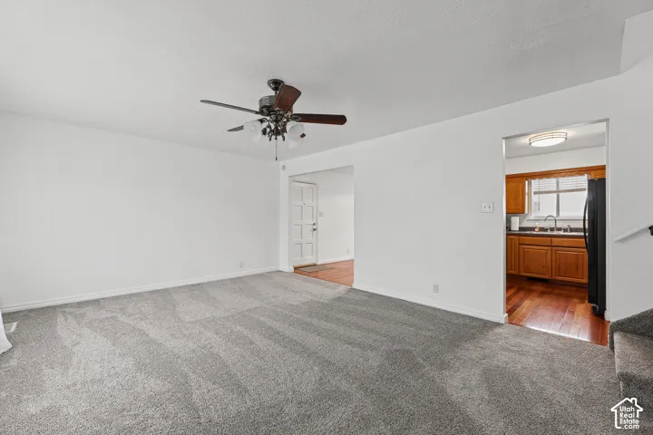 Spacious living area featuring neutral carpeting and a ceiling fan