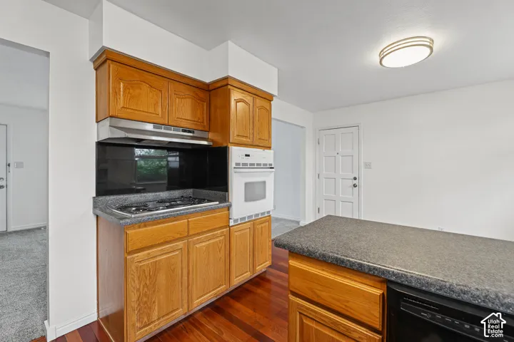 Wood-finish flooring, wood cabinetry, built-in oven, built-in gas cooktop, and a stainless steel range hood