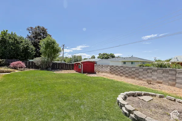 Expansive lawn area featuring a red utility shed, a decorative stone fire pit, and a segmented block retaining wall