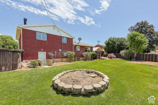 Expansive green lawn featuring a stone-edged fire pit, a red brick exterior, and a wooden privacy fence