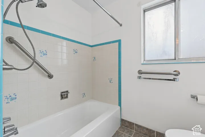 White bathtub with a tiled surround featuring blue accents and floral details, complemented by a handheld shower fixture