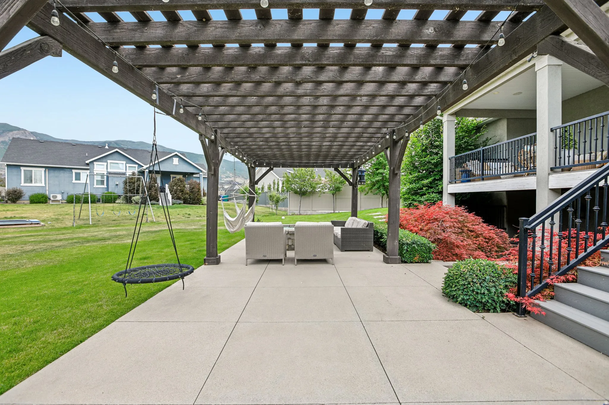 Expansive patio featuring a dark wood pergola with string lights, concrete flooring, and a manicured lawn