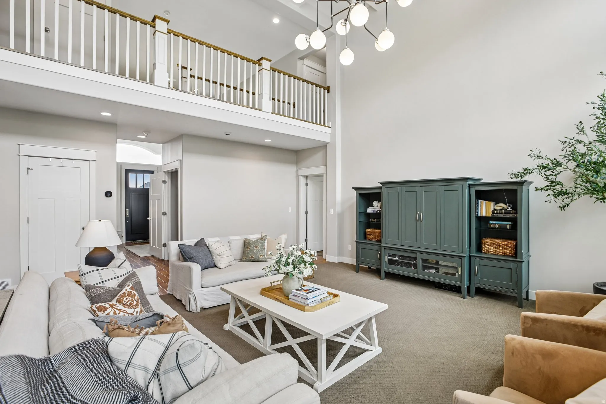 Vaulted ceiling living area featuring a second-story interior balcony with white balusters and wood-finish handrail, a contemporary multi-orb chandelier, and recessed lighting