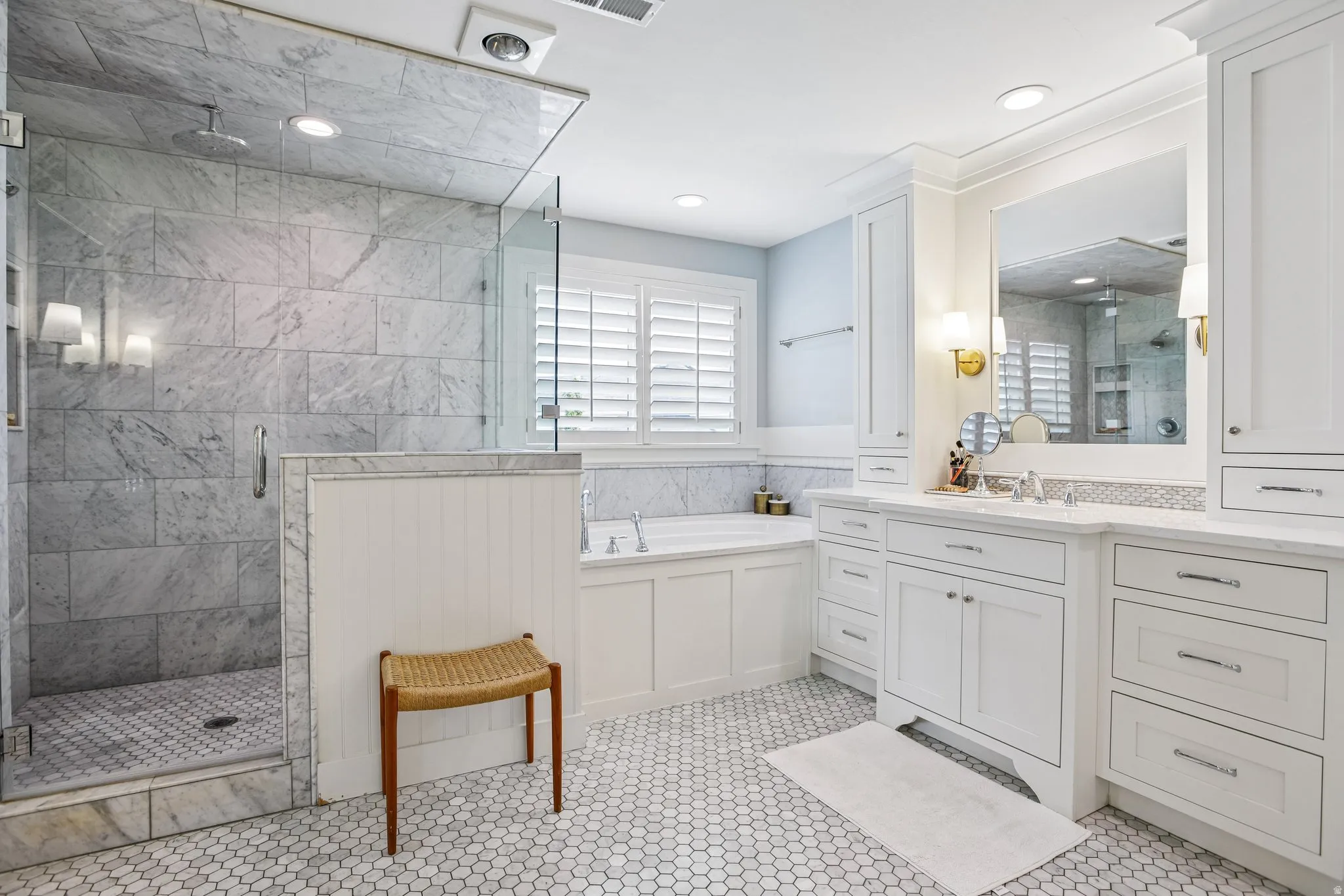 Bathroom featuring a frameless glass shower enclosure with tiled walls, a built-in soaking tub, extensive white cabinetry with integrated storage, dual sinks, and white hexagonal floor tiling