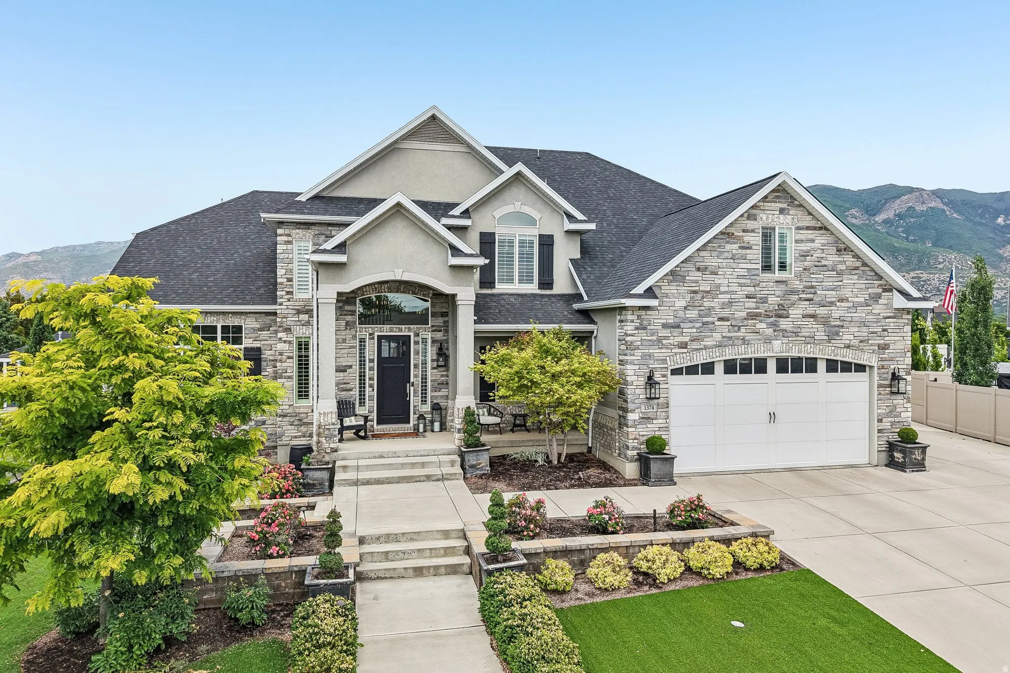 Stately stone and stucco exterior featuring a prominent arched entryway, a paved driveway, an attached two-car garage, mature landscaping, and a mountain backdrop