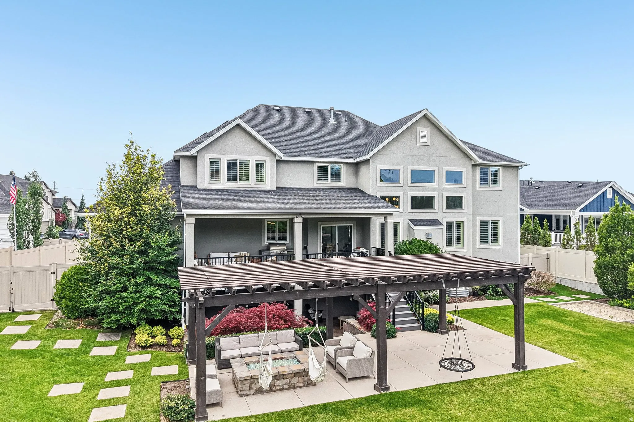Expansive rear patio featuring a wooden pergola, fire pit, and concrete pavers