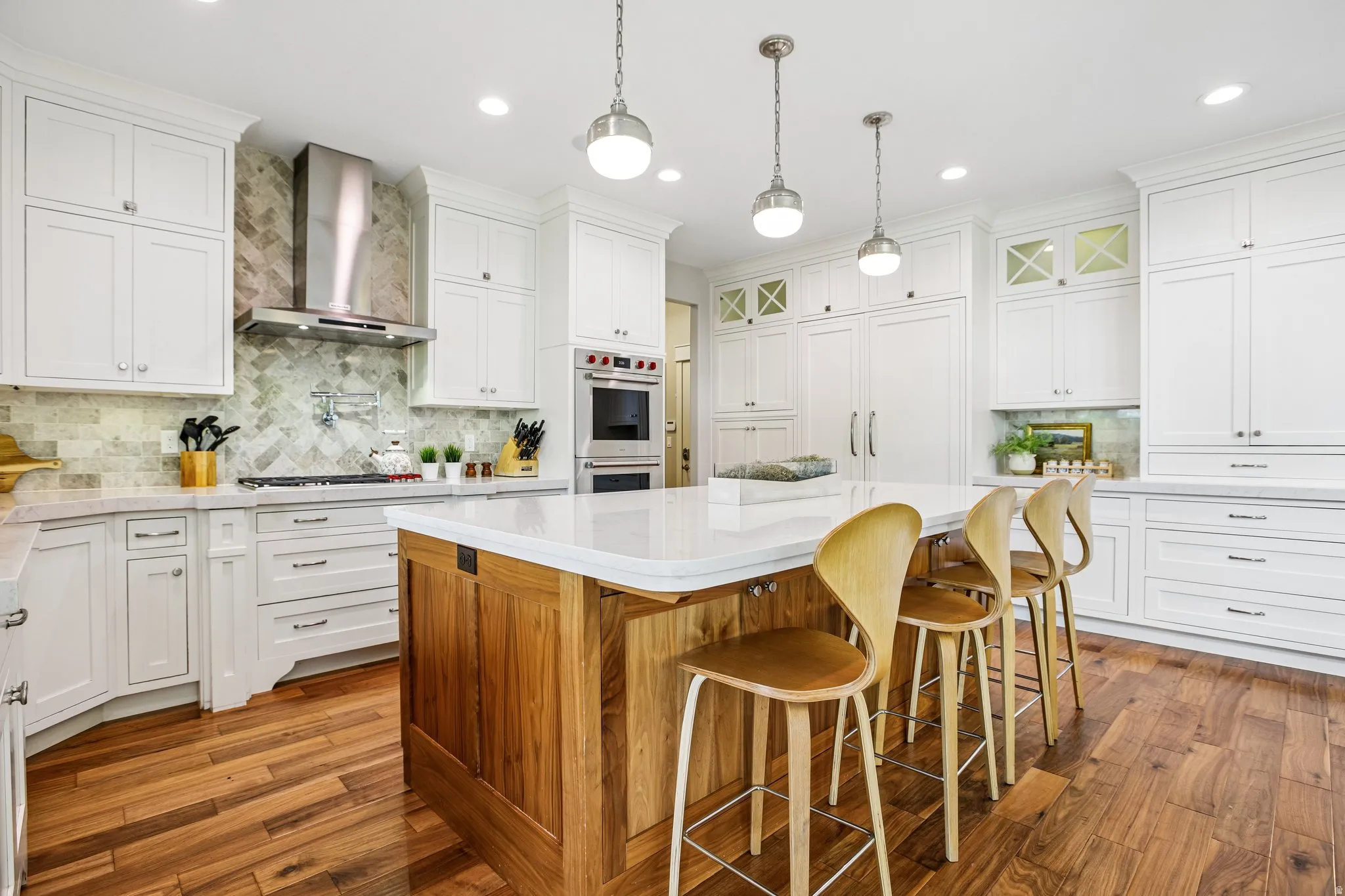 Spacious kitchen featuring a wood-finish island with seating, white shaker cabinetry, herringbone tile backsplash, integrated appliances, and wood-finish flooring