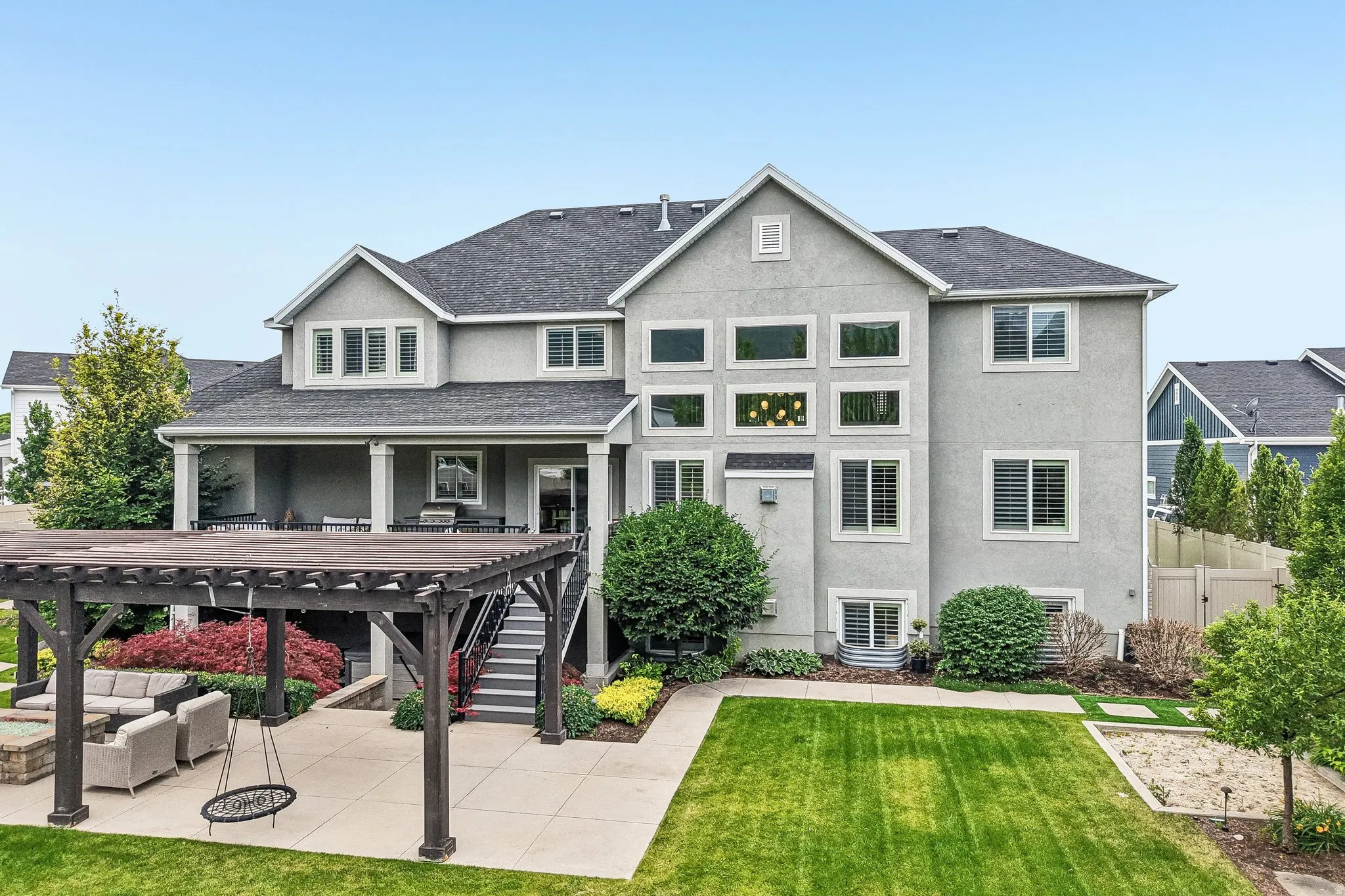 Rear exterior featuring a multi-level stucco facade, covered patio, outdoor pergola, and a manicured lawn