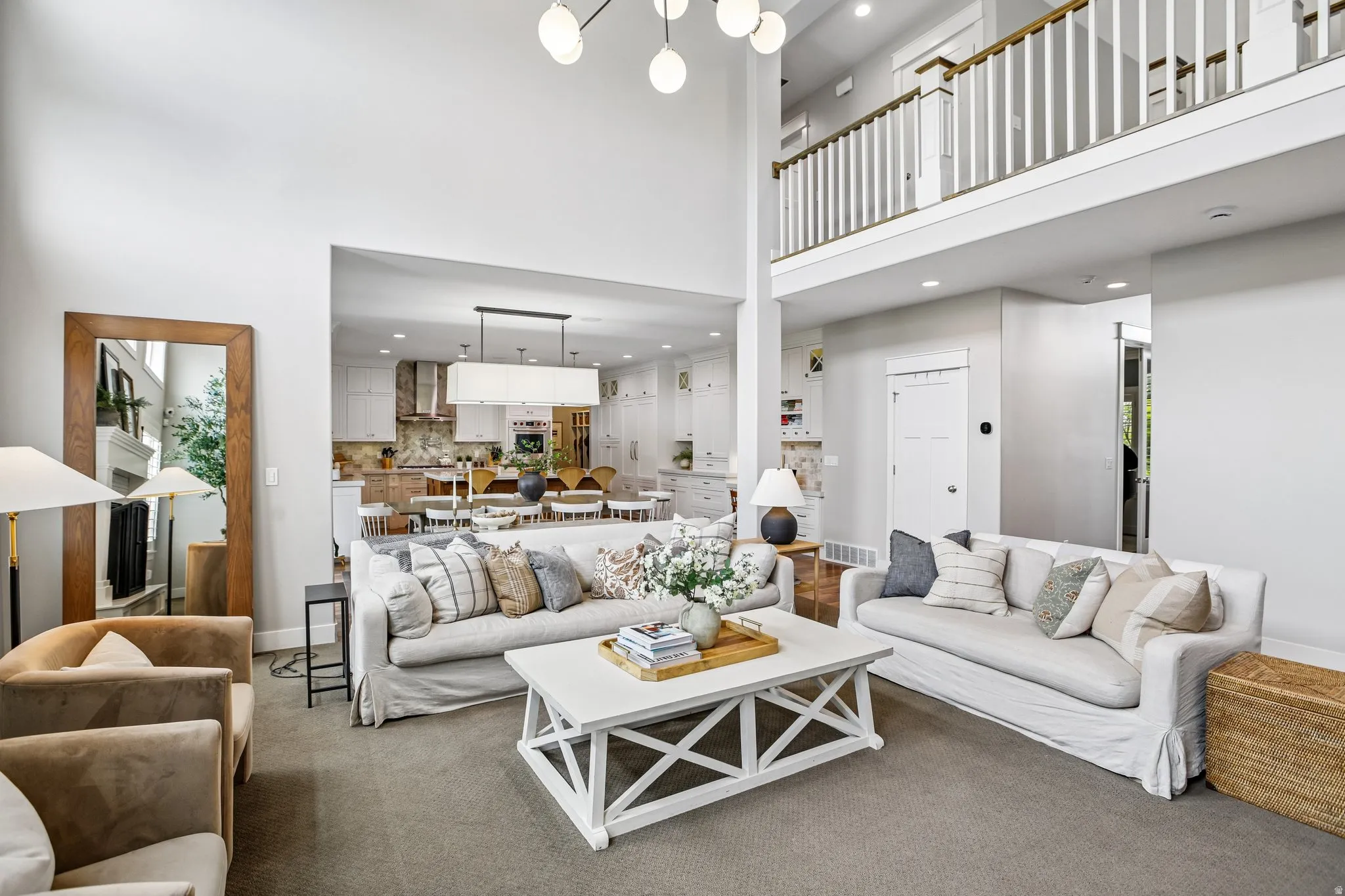 Two-story living area with high ceilings, an upper-level balcony with white balusters, and a contemporary multi-globe chandelier