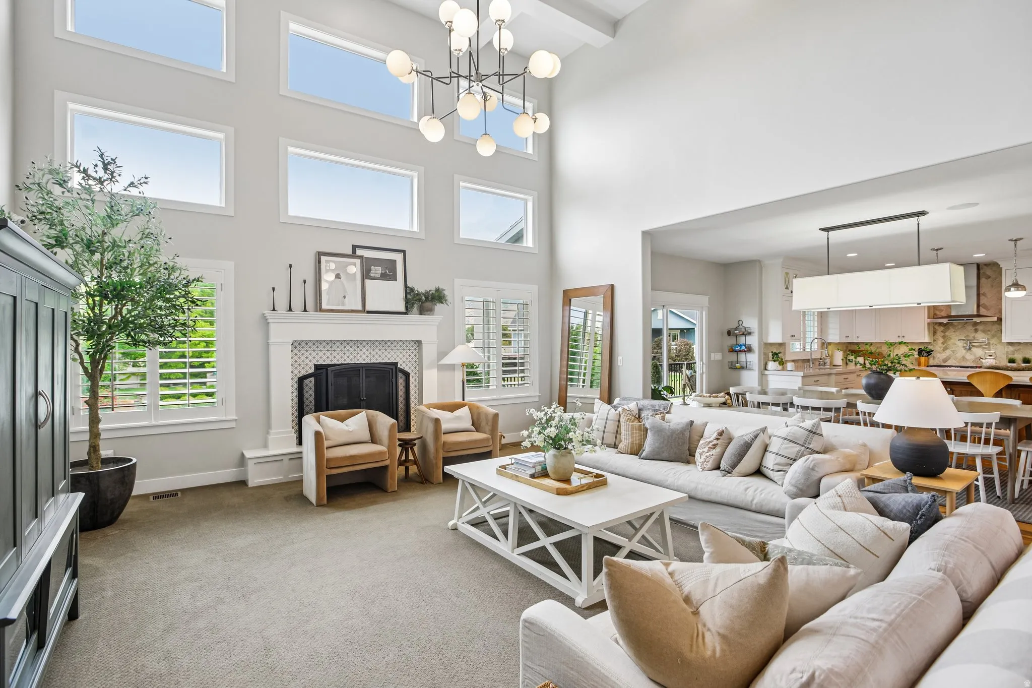 Double-height living space featuring extensive upper-level transom windows, a central chandelier, and a fireplace with a decorative tile surround and mantel
