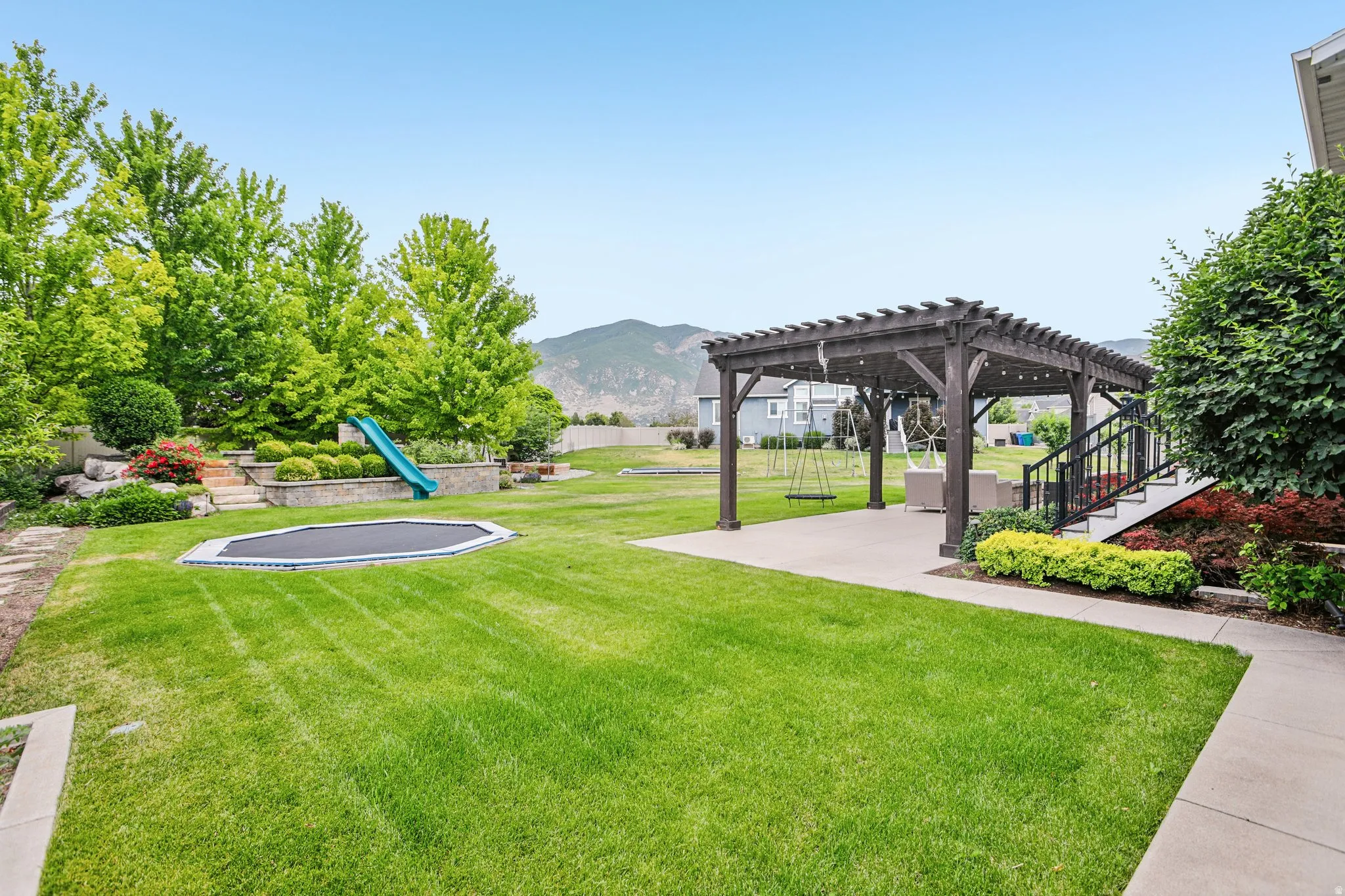 Expansive backyard featuring a large green lawn, concrete patio, and a dark wood pergola