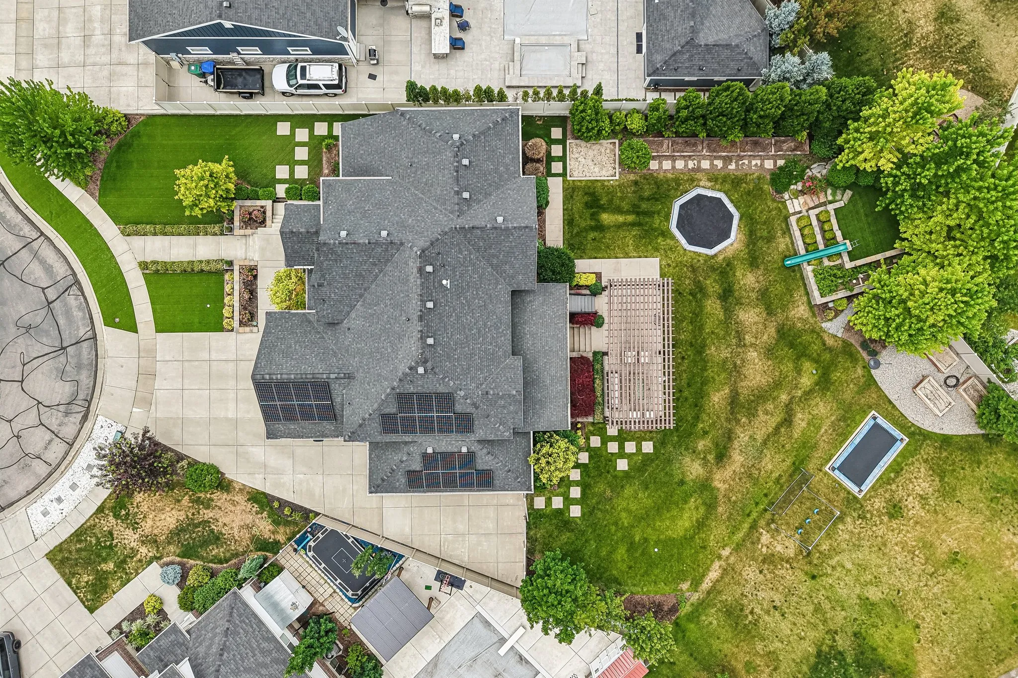 Expansive property featuring a multi-level residence with solar panels, a large paved driveway, and a spacious green lawn