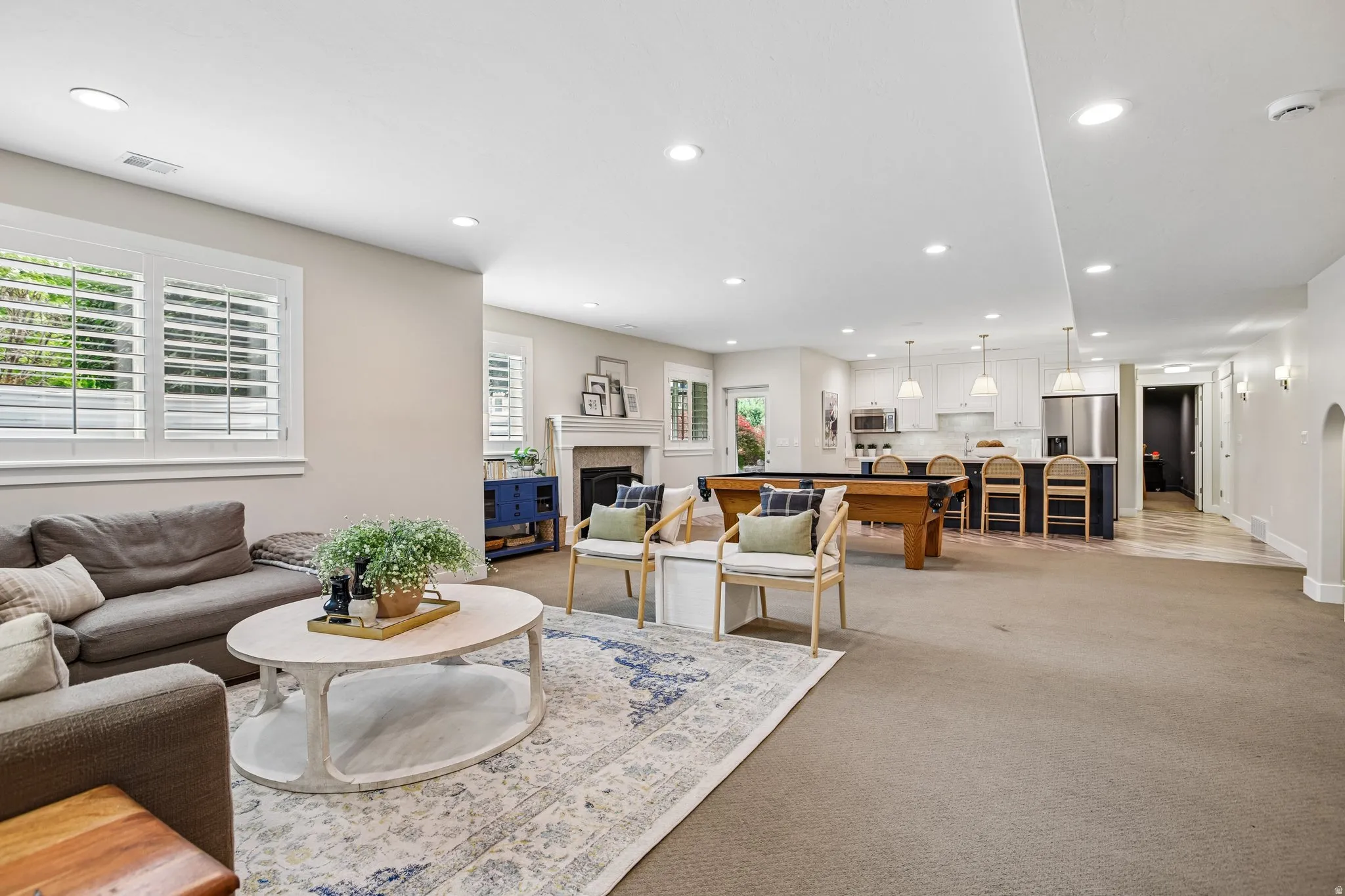 Open-concept living area featuring recessed lighting, plantation shutters, a kitchen island with pendant lighting, stainless steel appliances, and wood-finish flooring