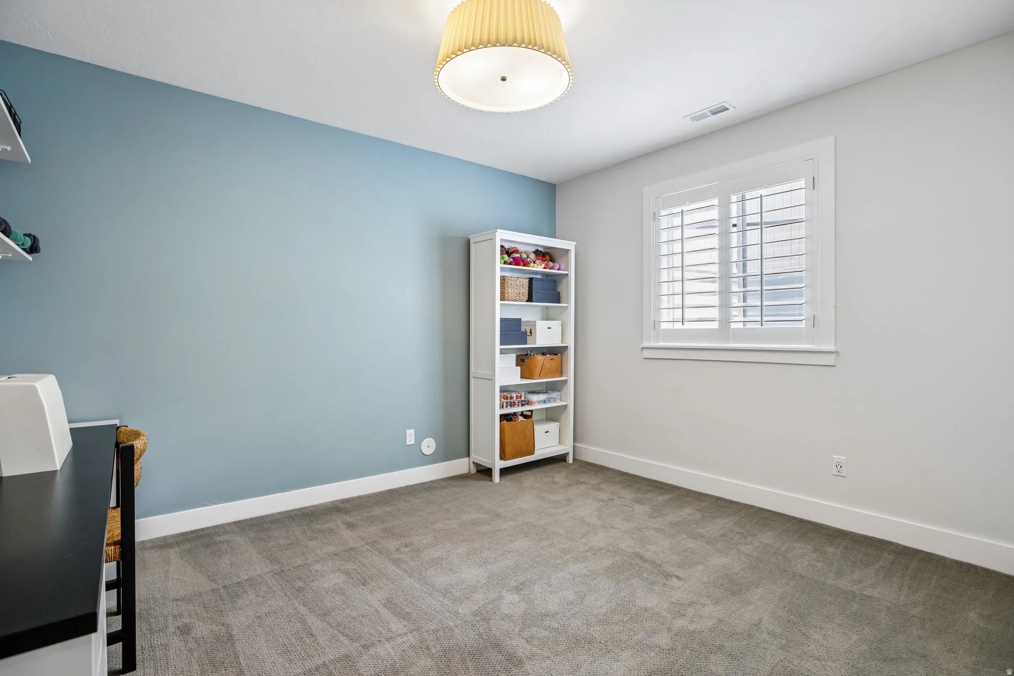Carpeted room featuring a window with white plantation shutters and white trim, a built-in shelf unit, and a blue accent wall