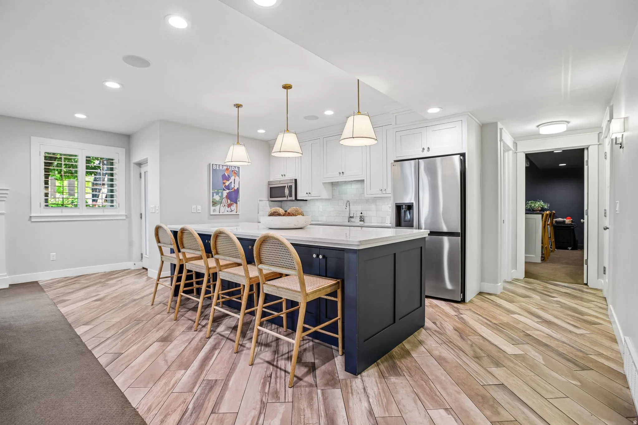 Kitchen featuring a dark-toned island with a light-colored countertop, three pendant lights, stainless steel appliances, white cabinetry, and wood-finish flooring