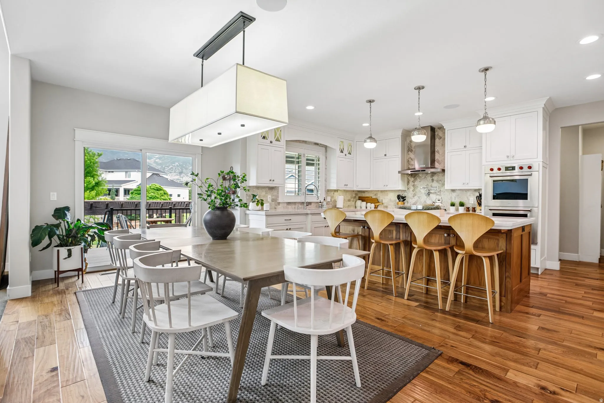 Open-concept kitchen and dining area featuring wood-finish flooring, white cabinetry, a kitchen island with seating, stainless steel appliances, and sliding glass doors opening to an outdoor deck