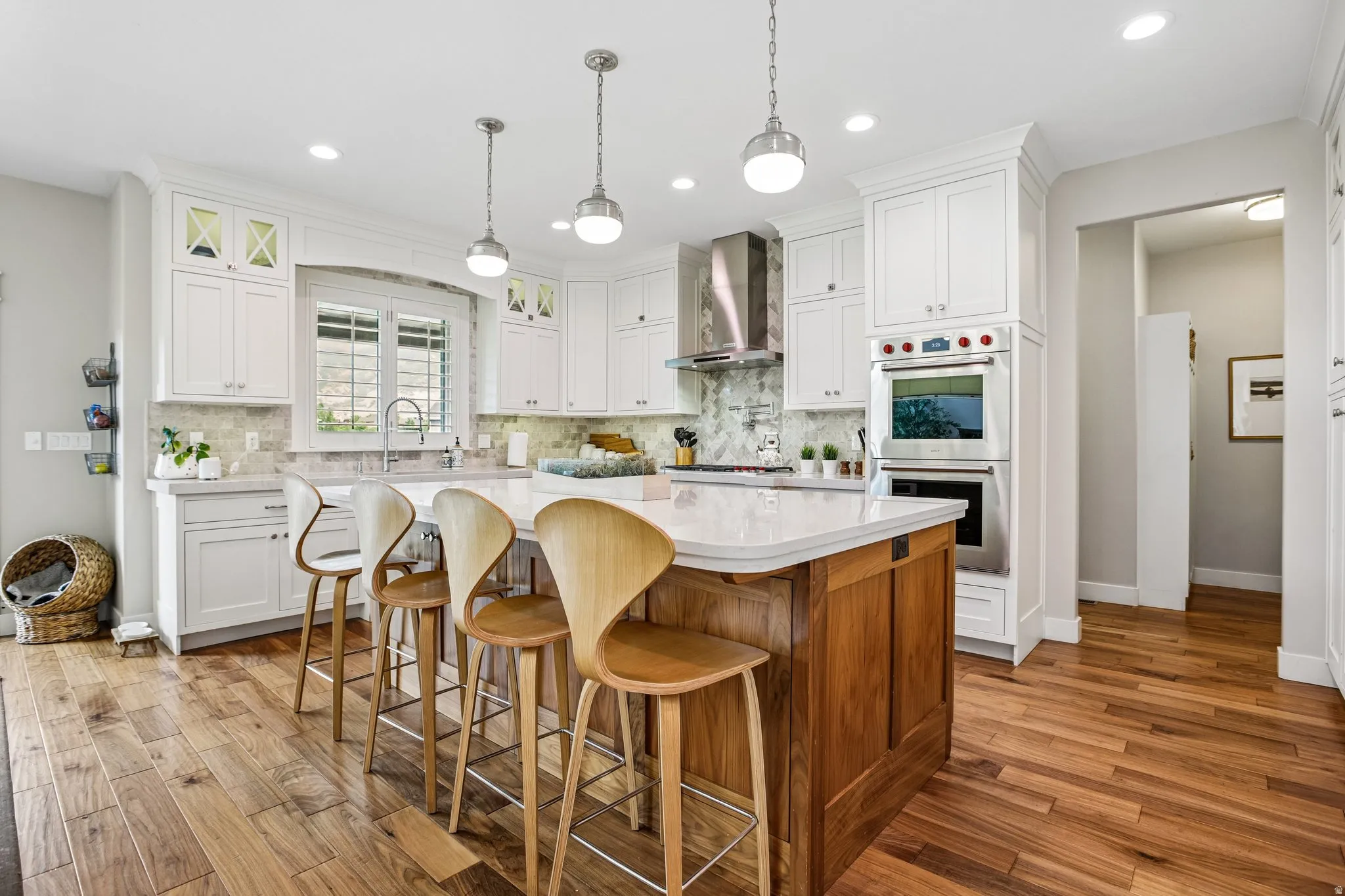 Kitchen featuring a large central island with seating, white cabinetry, integrated stainless steel appliances, wood-finish flooring, and pendant lighting
