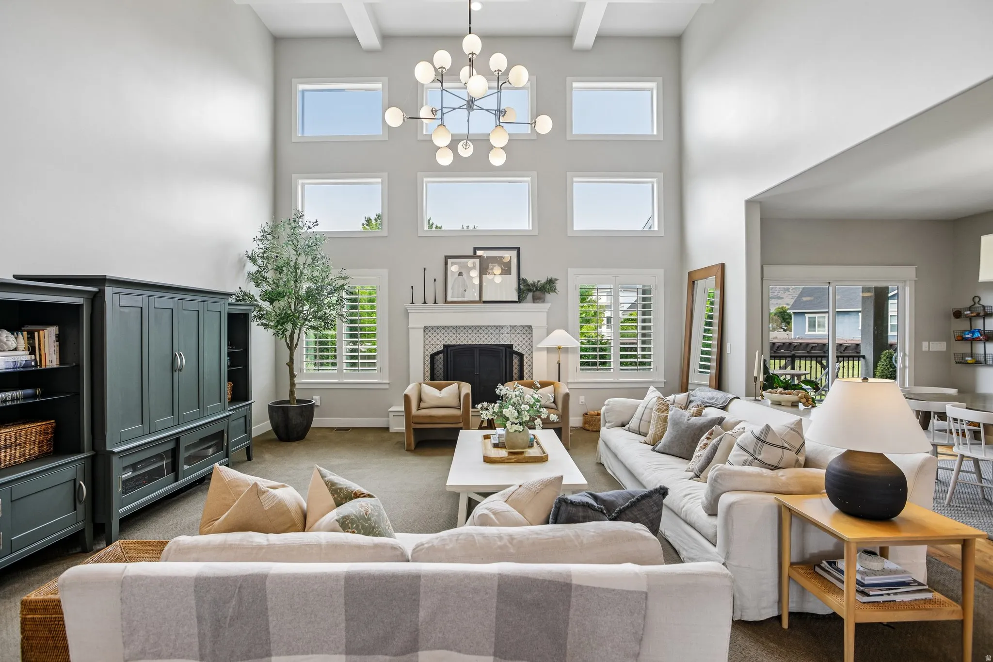 Two-story living area featuring a fireplace with a decorative tile surround and white mantel, a multi-pane window configuration, white window shutters, a contemporary chandelier, and recessed lighting