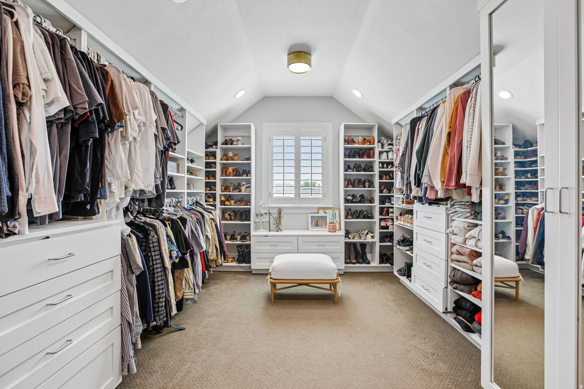 Expansive custom closet featuring extensive built-in storage, a window with plantation shutters, recessed lighting, and a full-length mirrored door