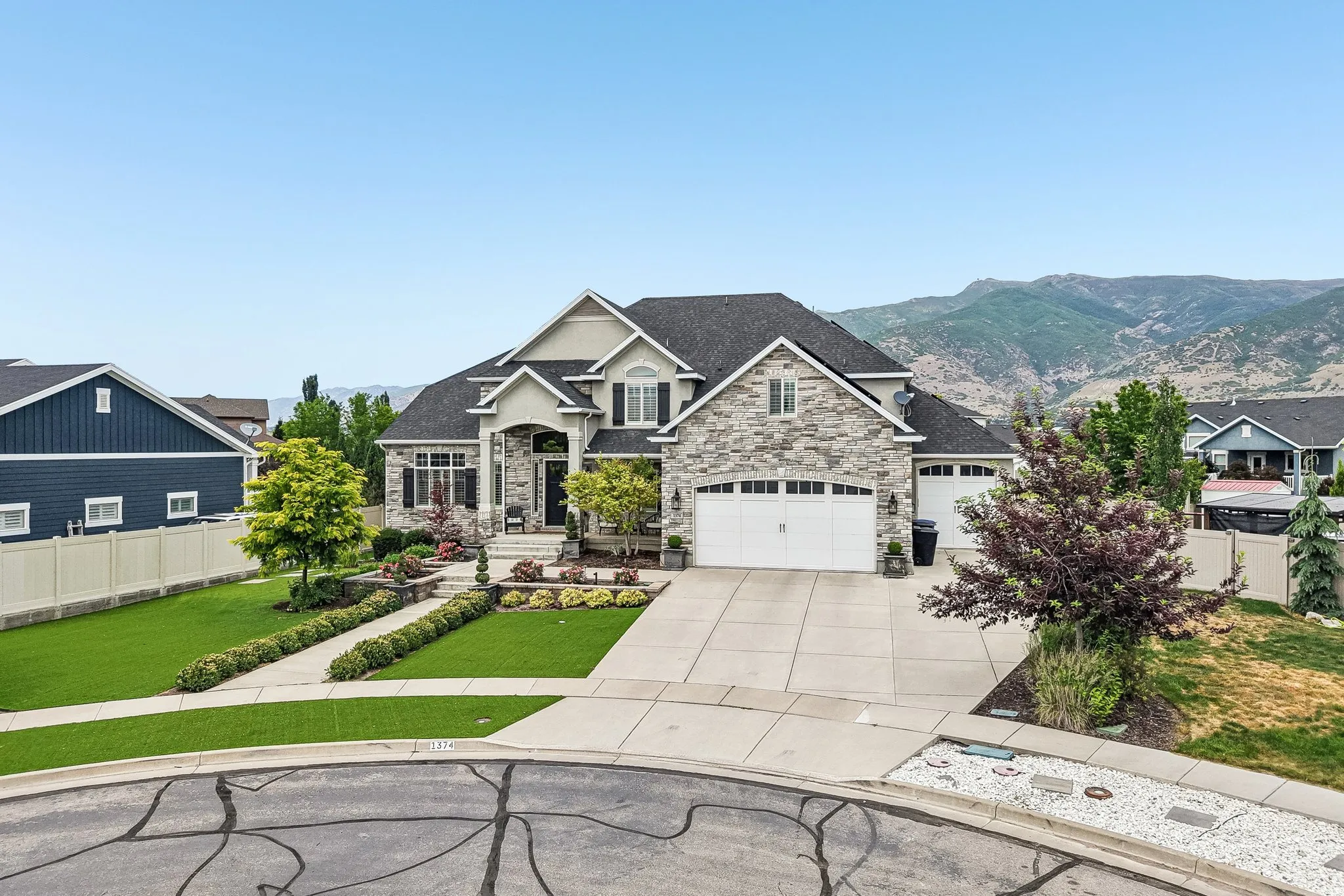Two-story residence featuring a stone and stucco exterior, multi-car garage, and a large paved driveway