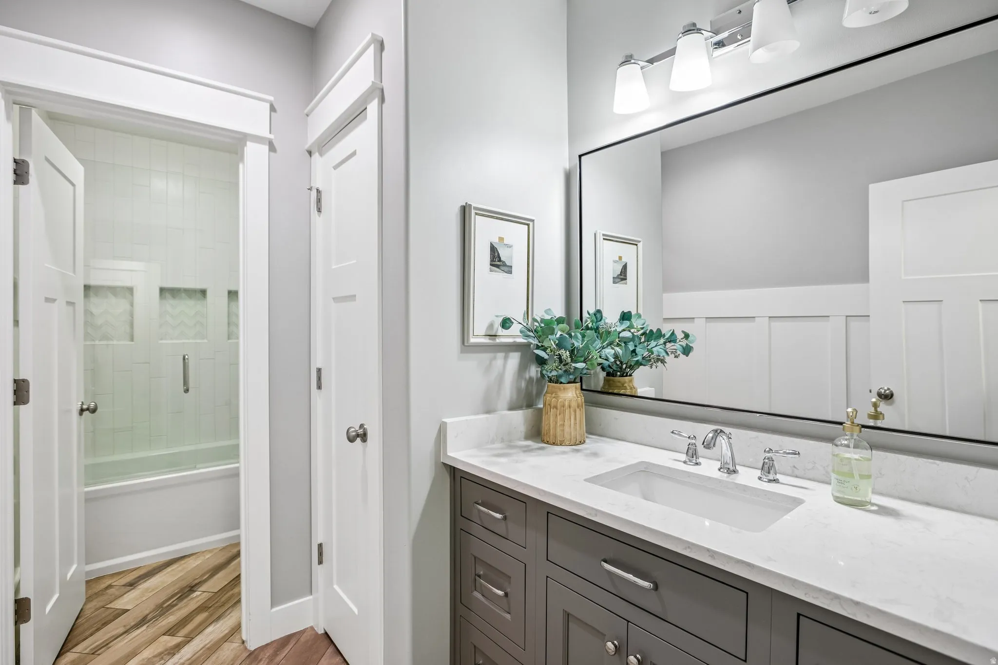 Bathroom featuring a rectangular undermount sink, a stone countertop, a large framed mirror, and a gray vanity with chrome hardware