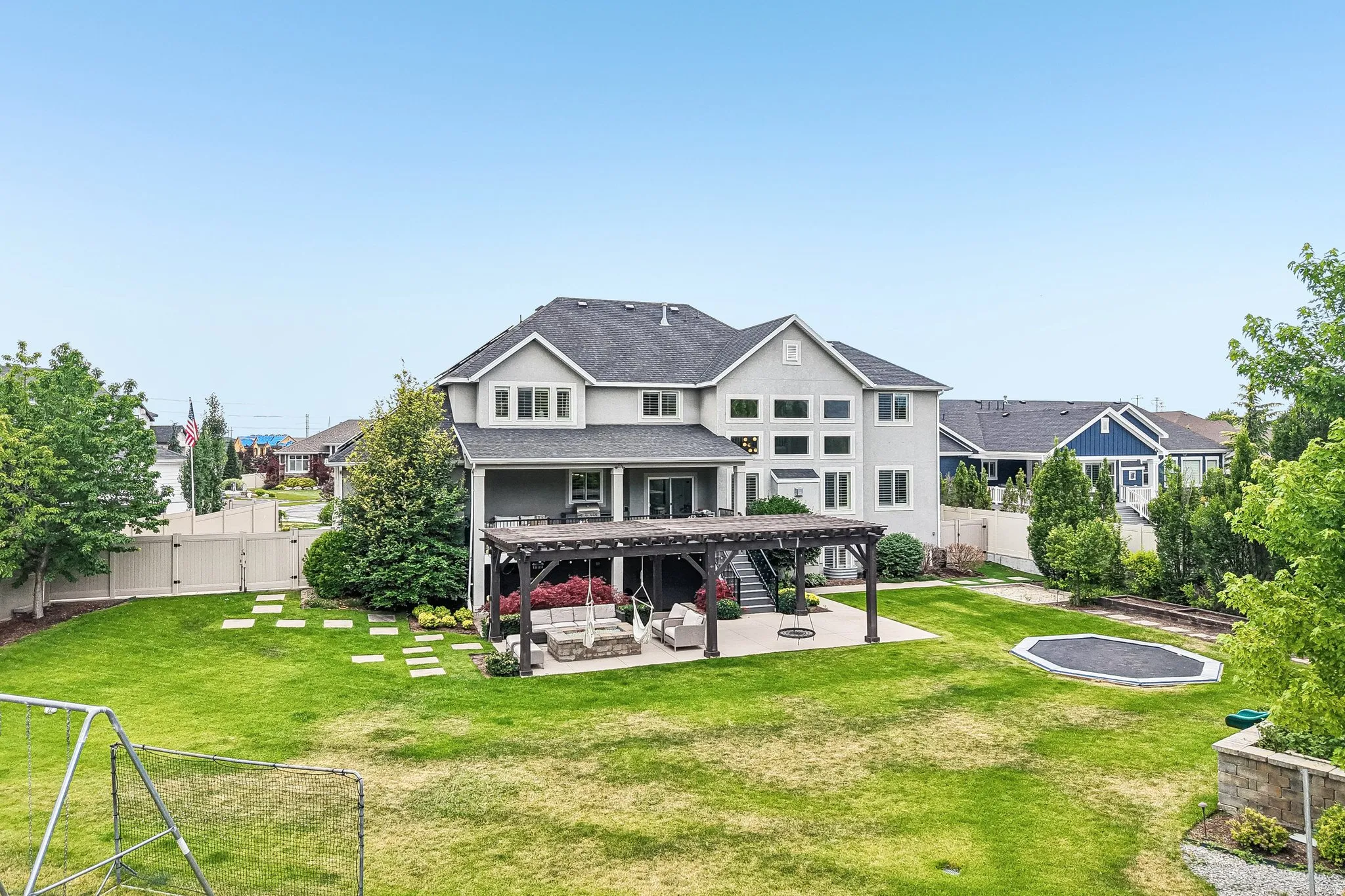 Spacious rear exterior featuring a two-story residence with multiple windows, a covered patio with a dark wood pergola, and a concrete patio space
