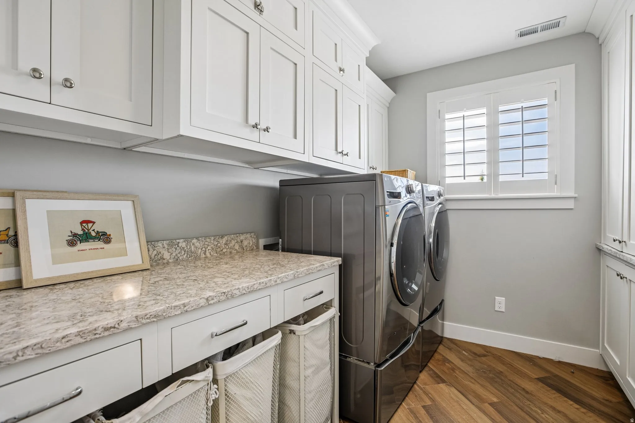 Laundry area featuring wood-finish flooring, white shaker-style cabinetry, and light-toned countertops