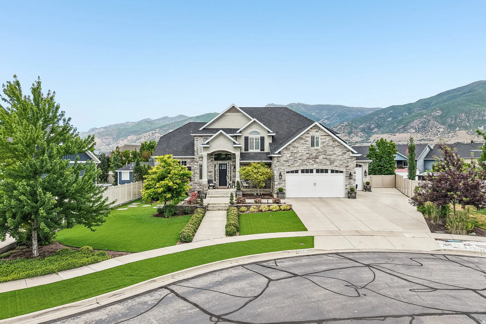Grand two-story residence featuring a stone and stucco exterior, prominent gable roofs, an attached two-car garage with white panel doors, and a concrete driveway