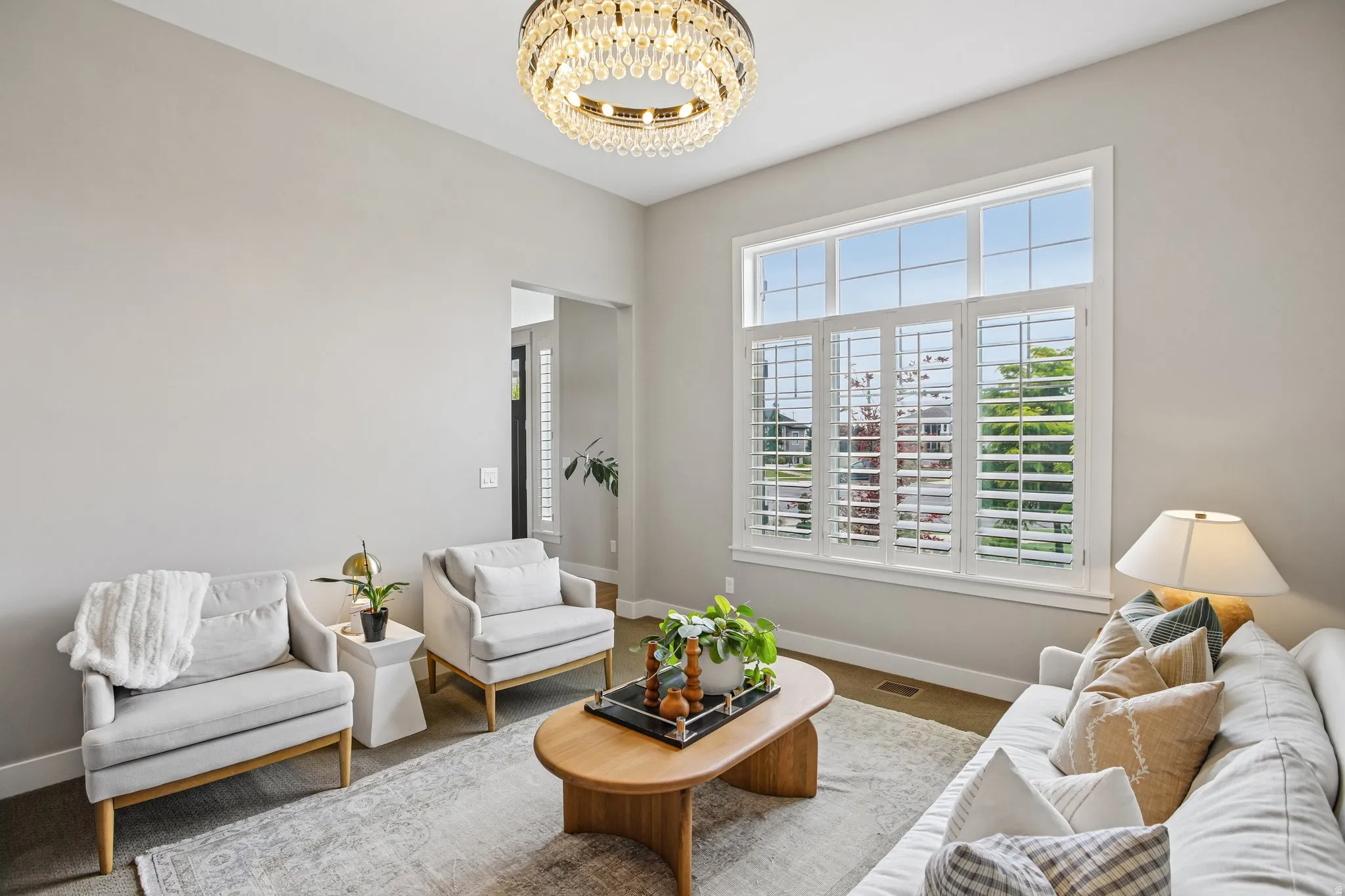 Living area featuring high ceilings, a prominent chandelier, and a large window with plantation shutters