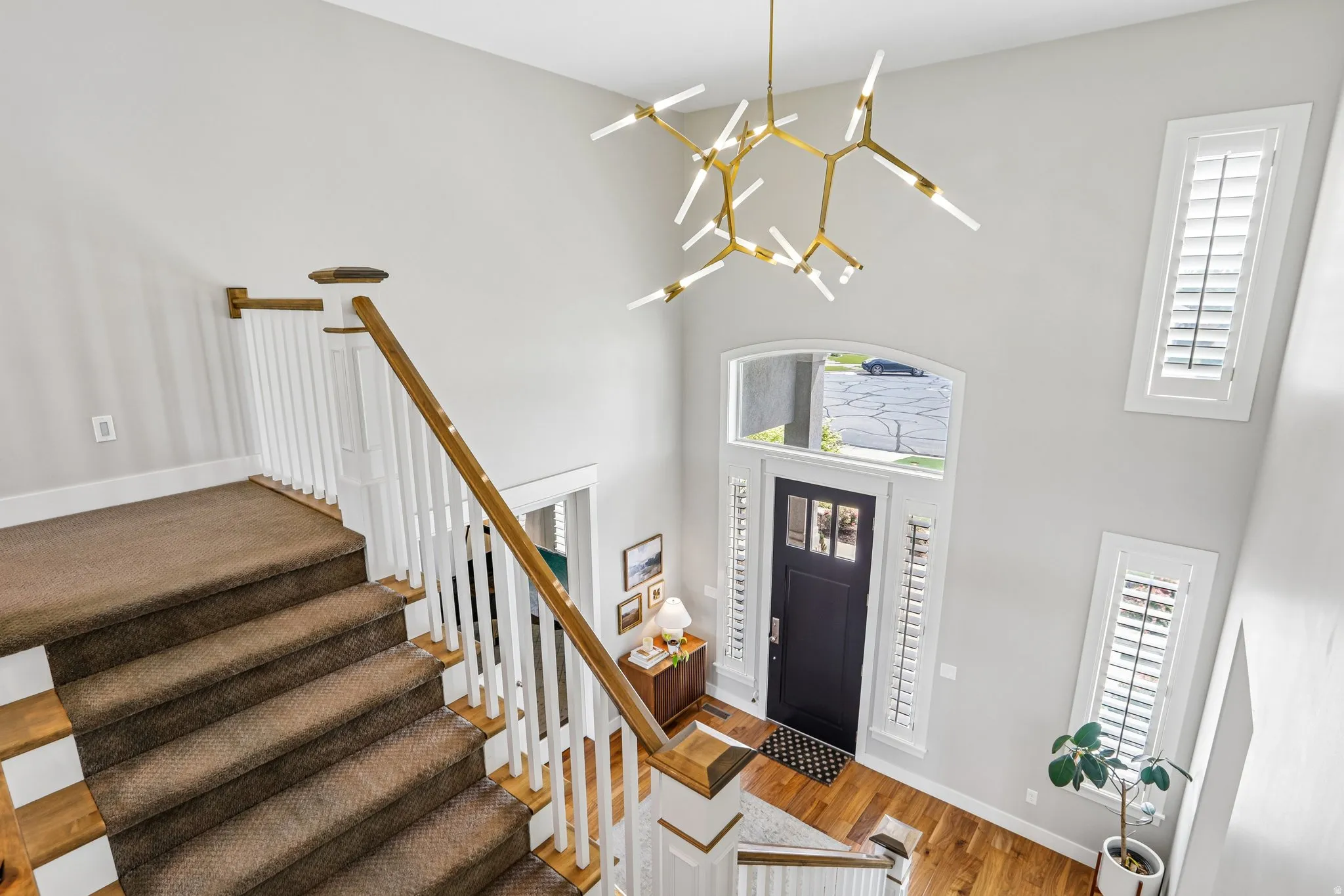 Two-story entryway featuring a modern chandelier, dark wood door with glass inserts, and hardwood flooring