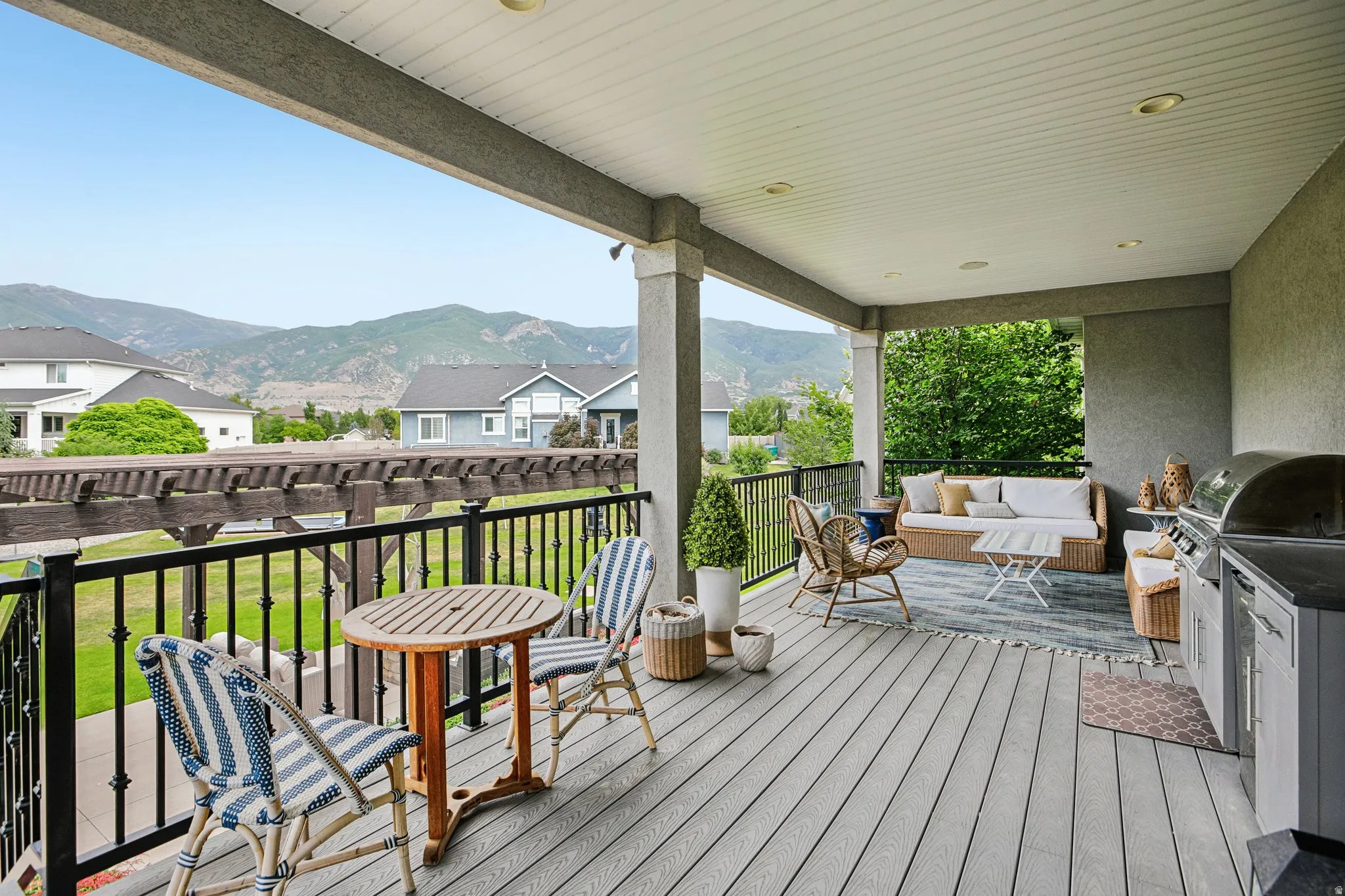 Expansive covered deck featuring composite decking, recessed lighting, a built-in outdoor kitchen with grill, and black wrought iron railings