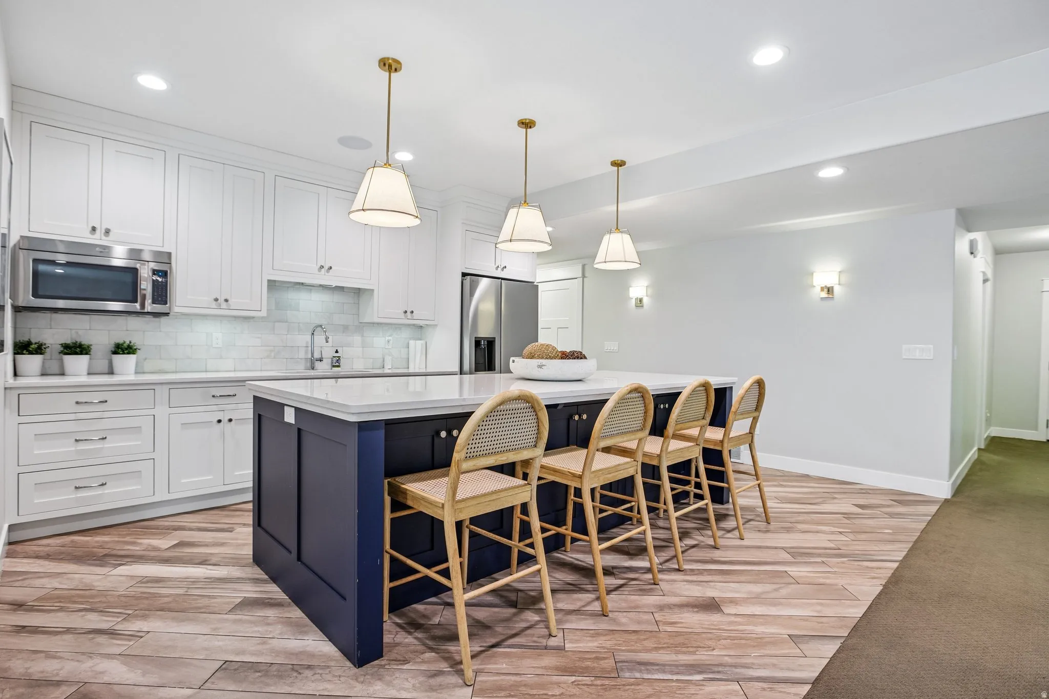 Gourmet kitchen featuring a large central island with seating, white shaker cabinetry, stainless steel appliances, and wood-finish flooring