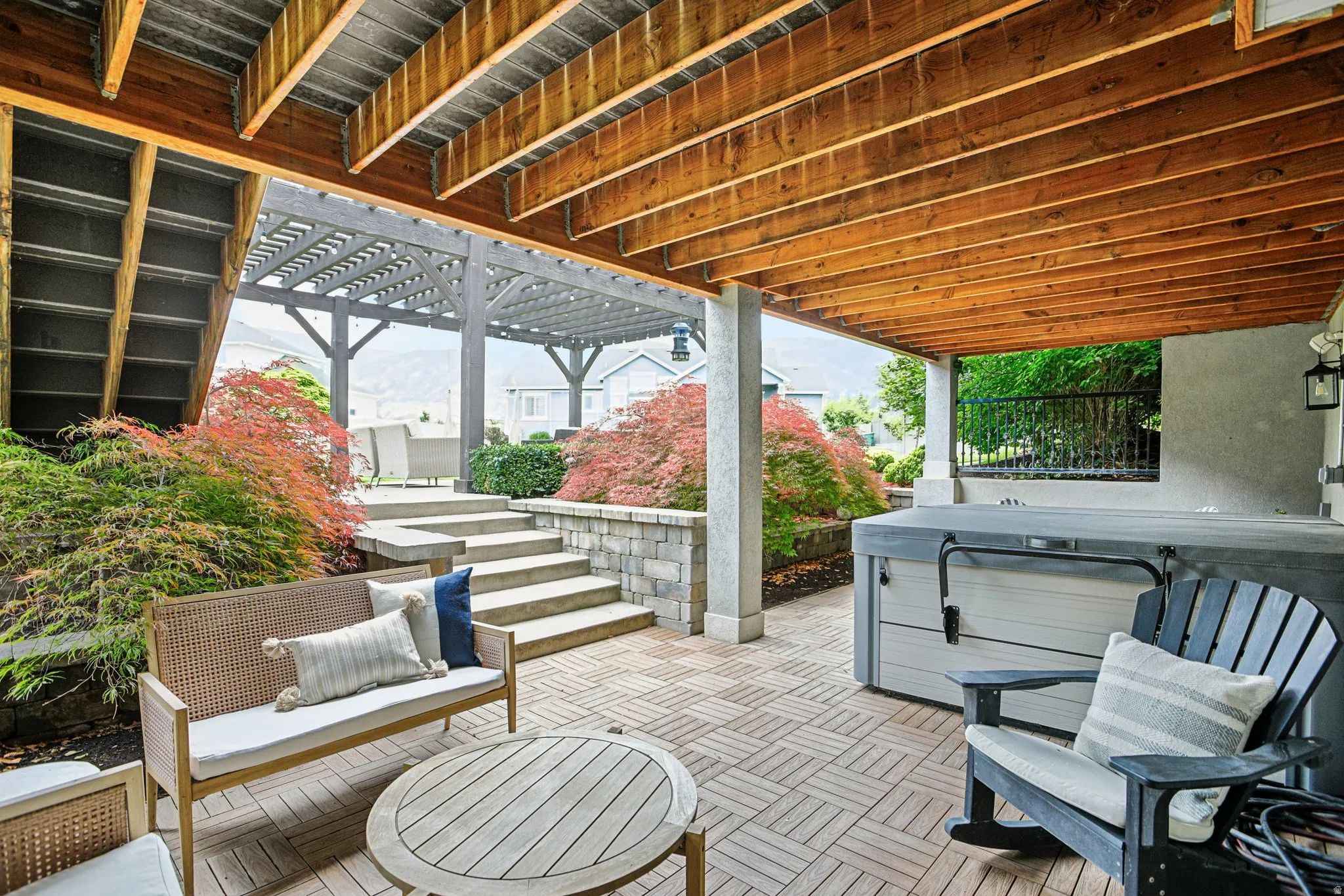 Covered patio with wood-finish ceiling, brick-patterned hardscaping, built-in spa, and stone-clad retaining wall