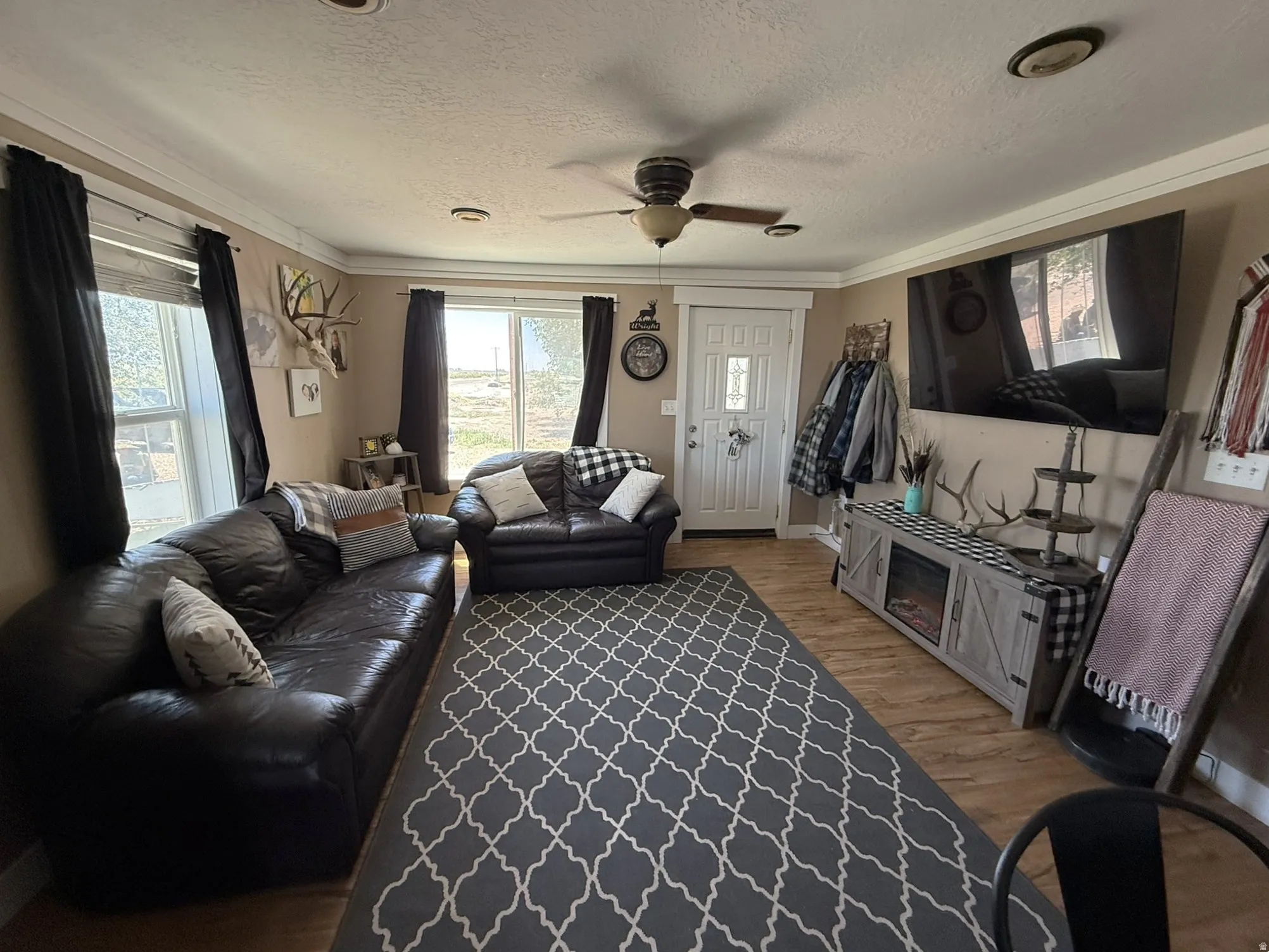 Inviting living area featuring wood-finish flooring, a ceiling fan with integrated lighting, and crown molding