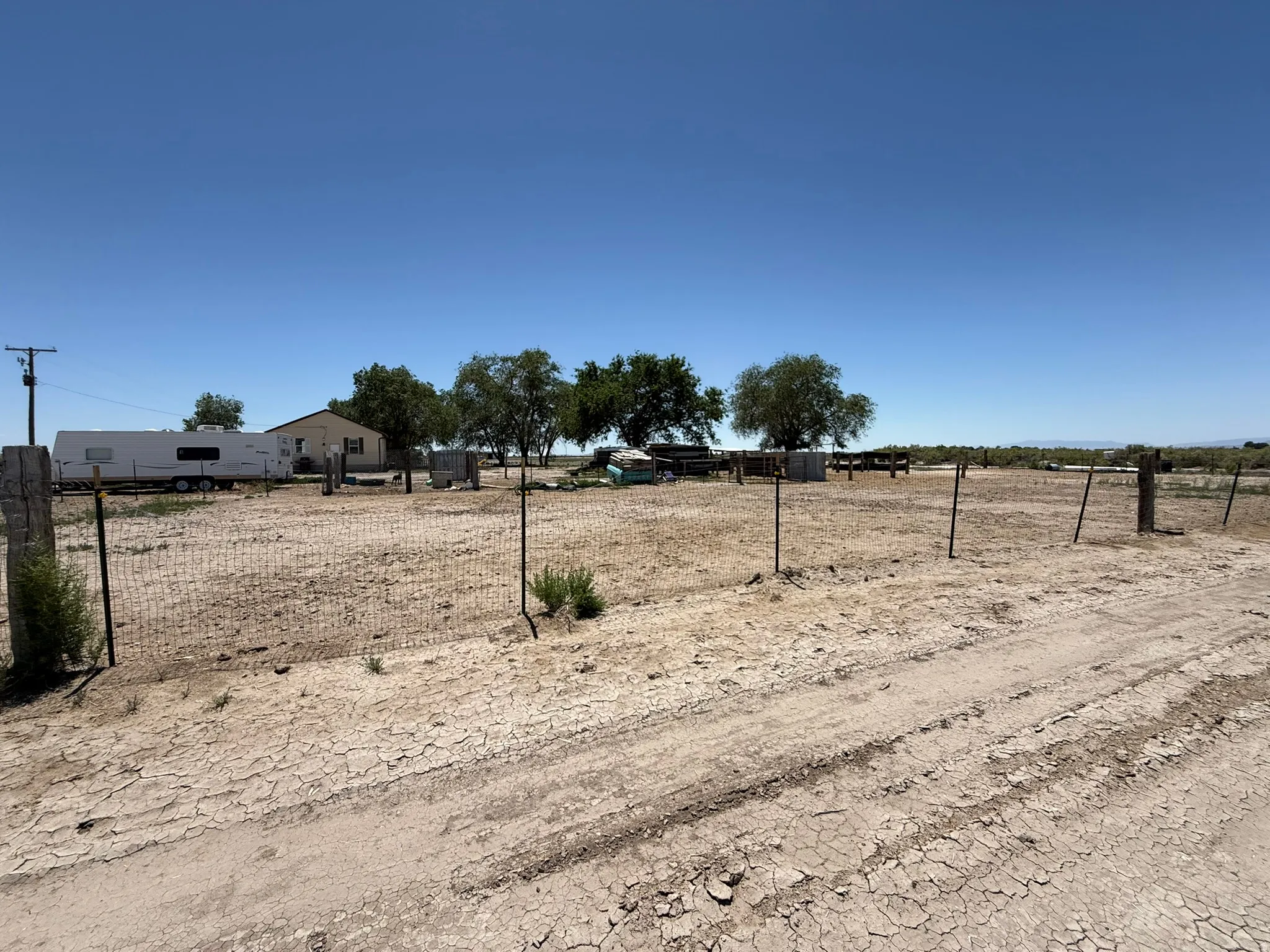 Expansive fenced lot featuring mature trees and a single-story residence in the background