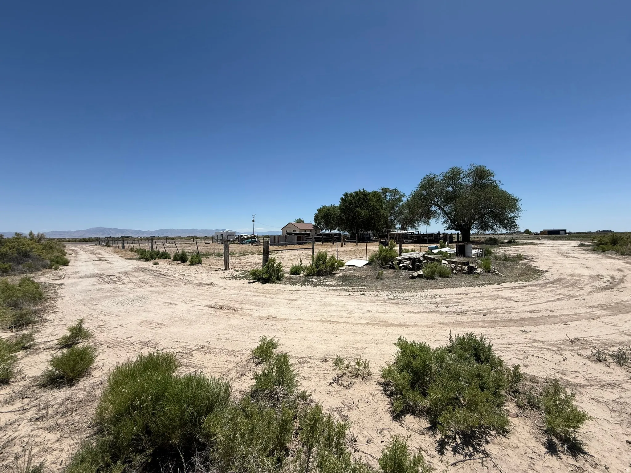 Expansive dirt driveway with a partial wooden fence and mature trees