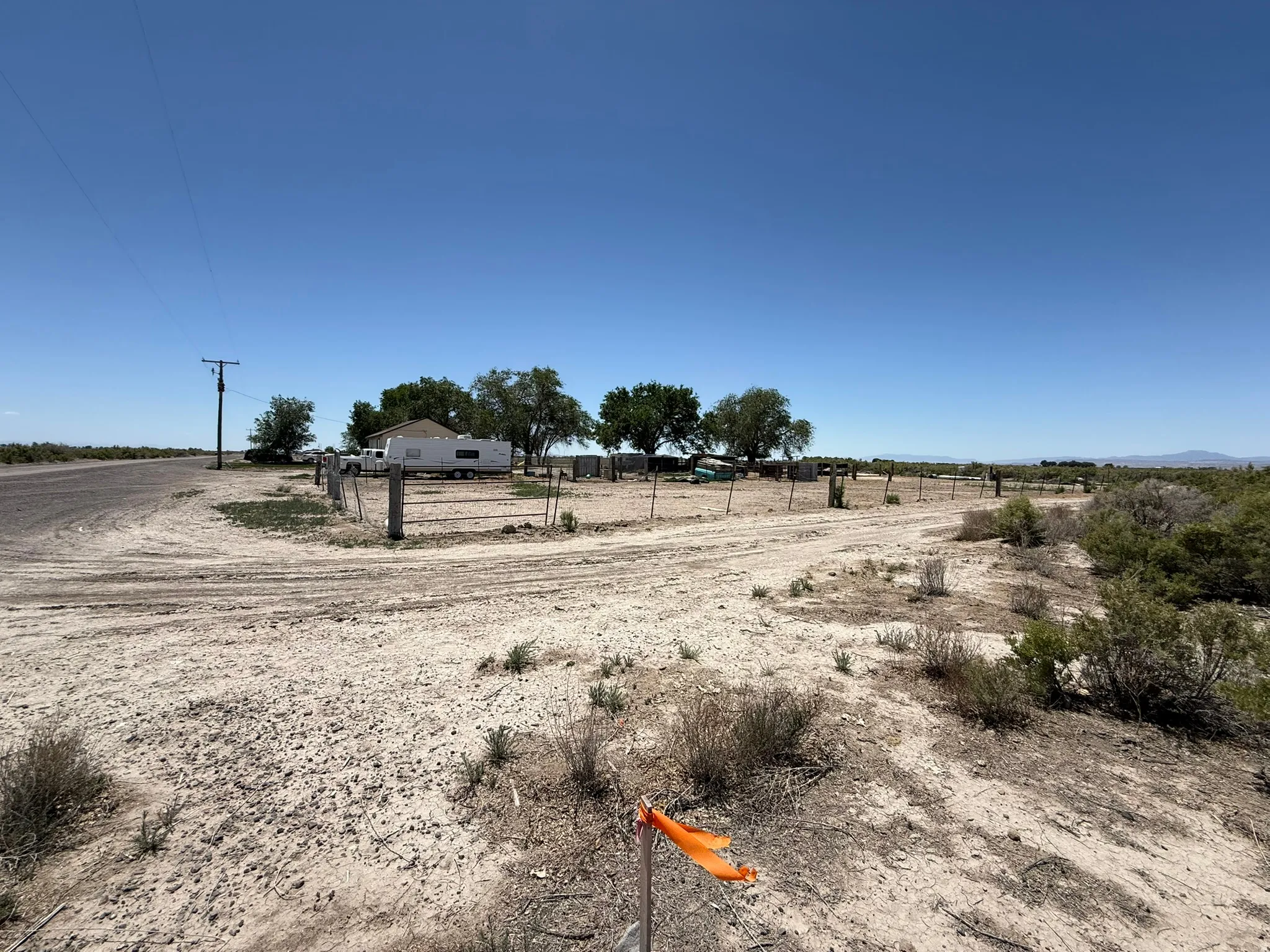 Expansive undeveloped land featuring a gravel road, natural desert foliage, and distant structures