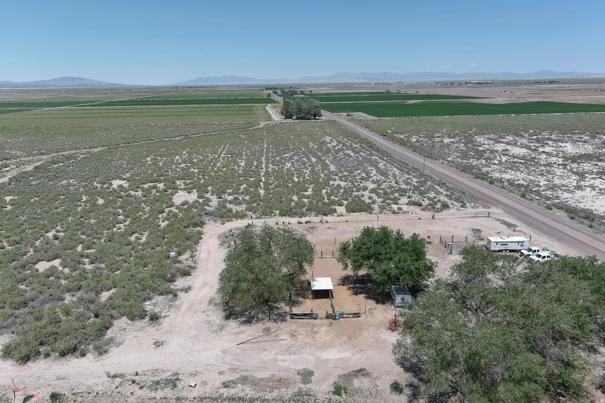 Expansive rural property featuring a long gravel driveway, a large fenced area, mature trees, and an open-sided shed