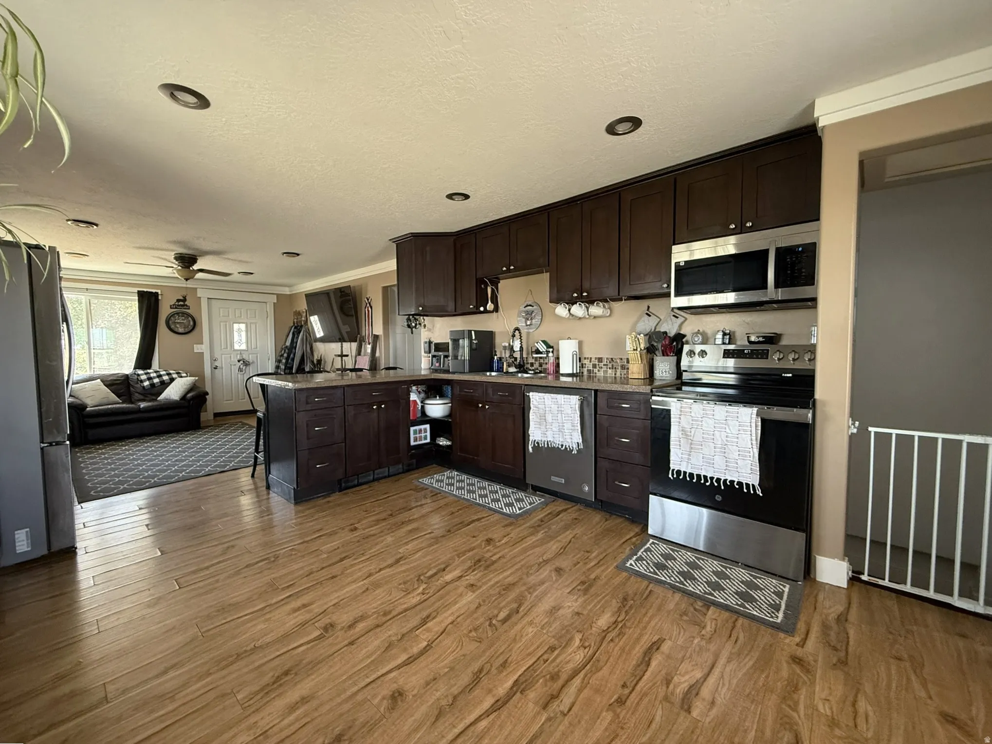 Open-concept kitchen featuring wood-finish flooring, dark wood cabinetry, stainless steel appliances, recessed lighting, and a kitchen island with seating