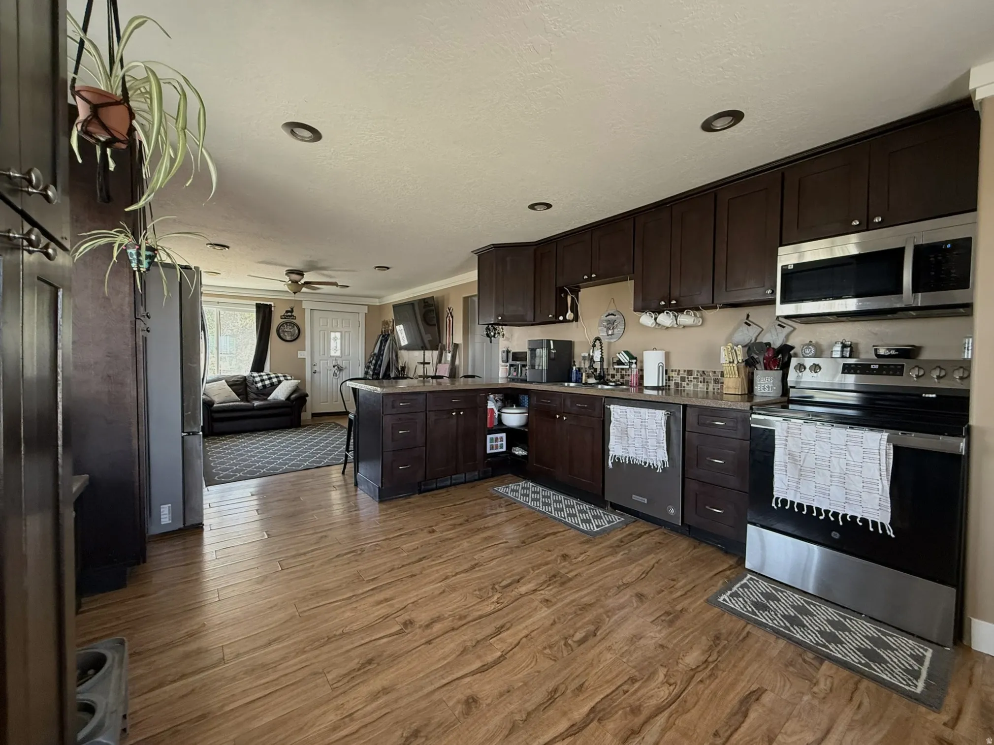 Open-concept kitchen featuring wood-finish flooring, dark wood cabinetry, stainless steel appliances, recessed lighting, and a kitchen island with counter seating