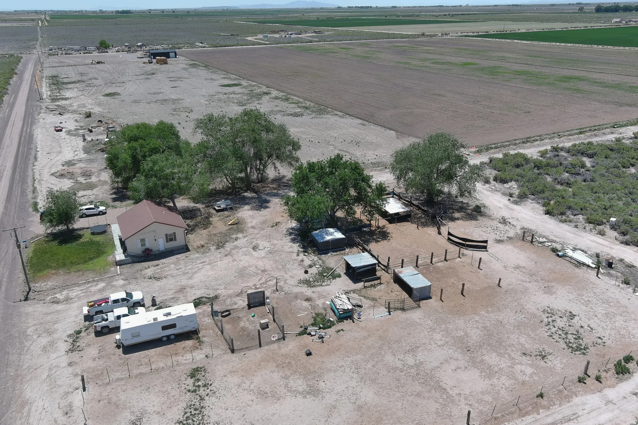 Expansive rural property featuring a main residence with a brown roof, multiple outbuildings, fenced areas, and mature trees