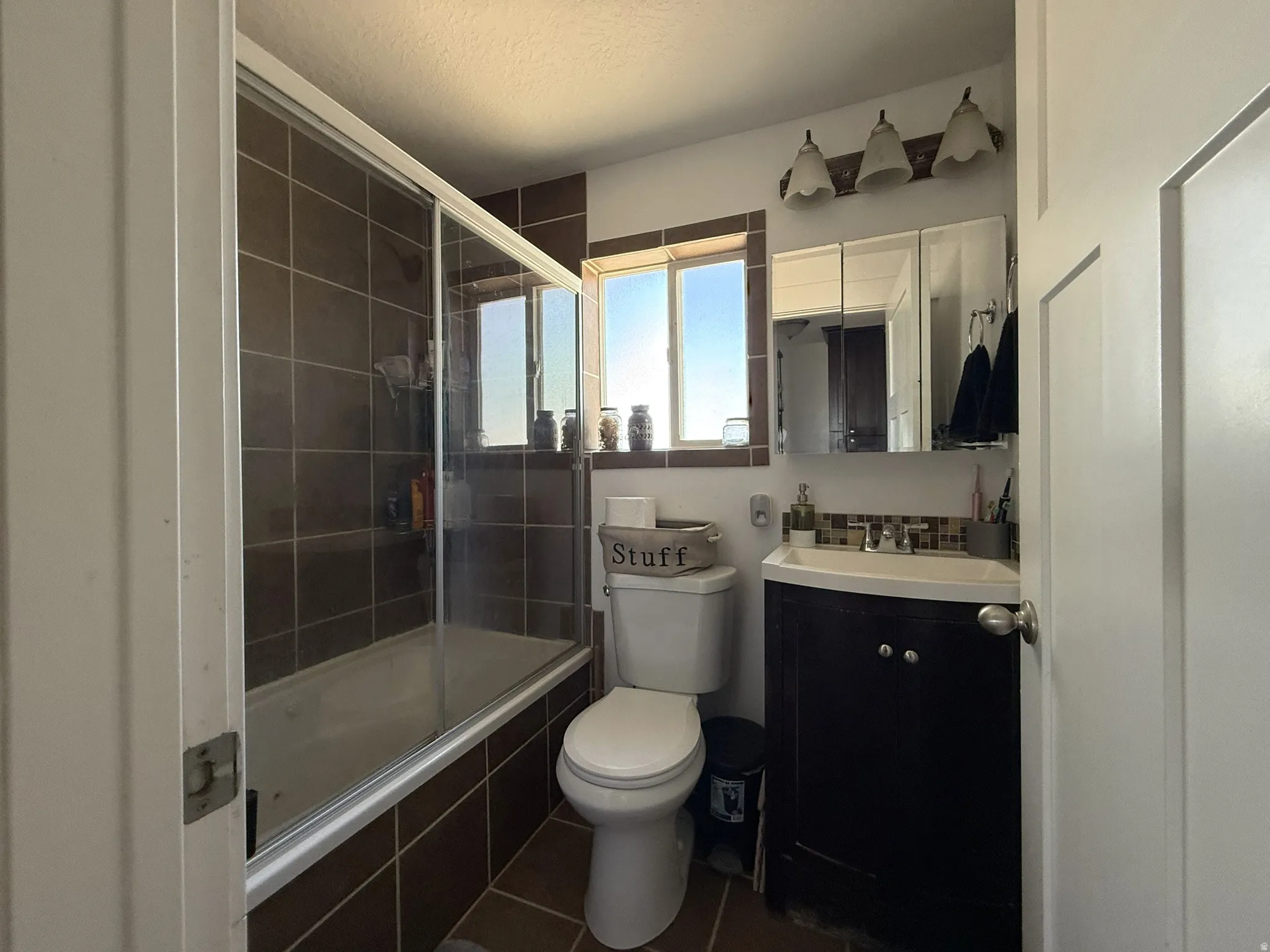 Bathroom featuring a full-size tub with sliding glass doors and brown tile surround