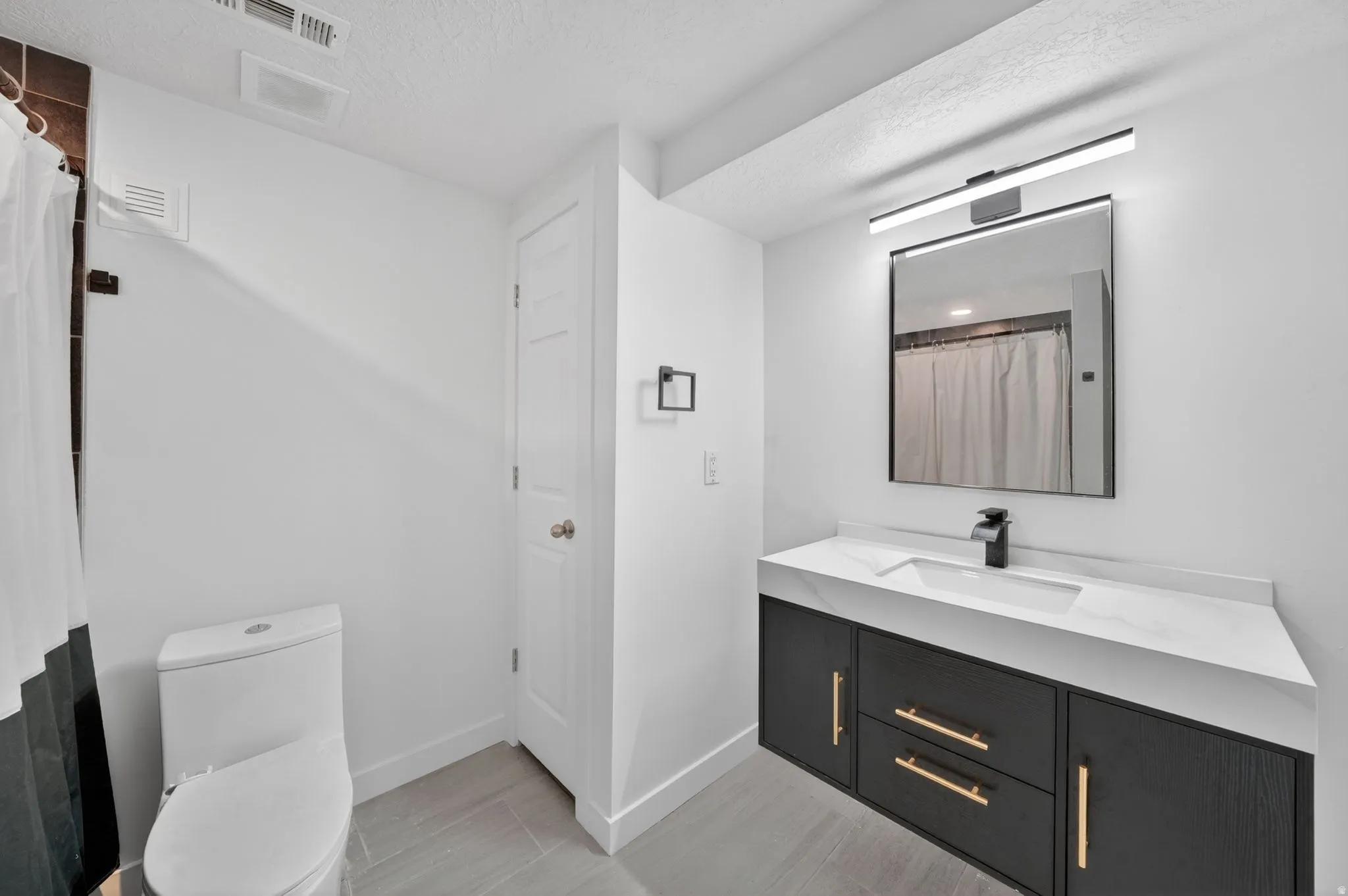 Bathroom featuring a modern floating vanity with gold-tone hardware, a white countertop with integrated sink, and a black-framed mirror with an overhead light fixture