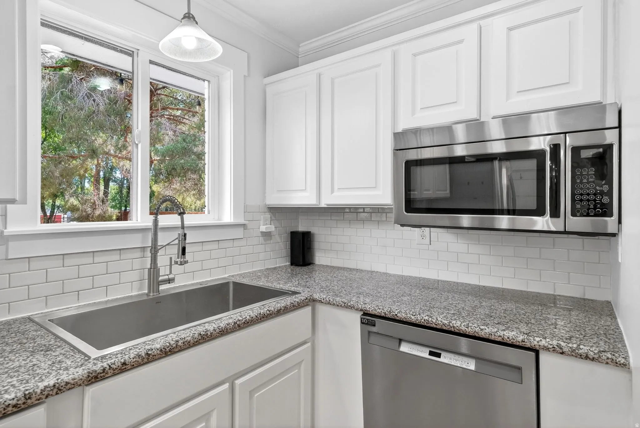 Kitchen features white shaker cabinetry, stainless steel appliances, granite countertops, a subway tile backsplash, and a large undermount sink with a gooseneck faucet
