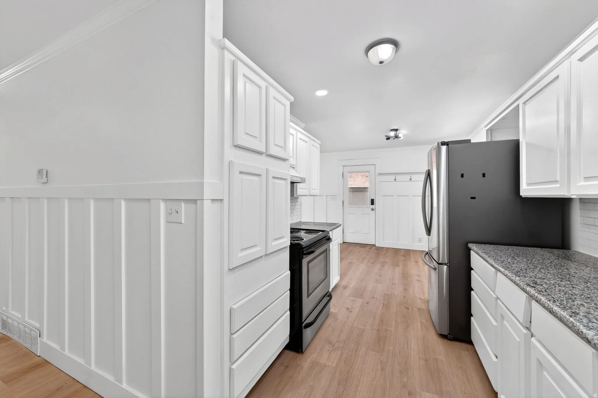 Kitchen featuring white shaker cabinetry, speckled countertops, stainless steel refrigerator, and wood-finish flooring