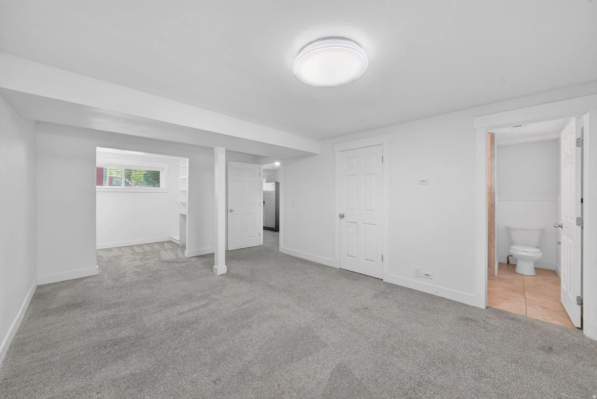 Expansive room featuring light gray carpet flooring, white walls, and a ceiling-mounted light fixture