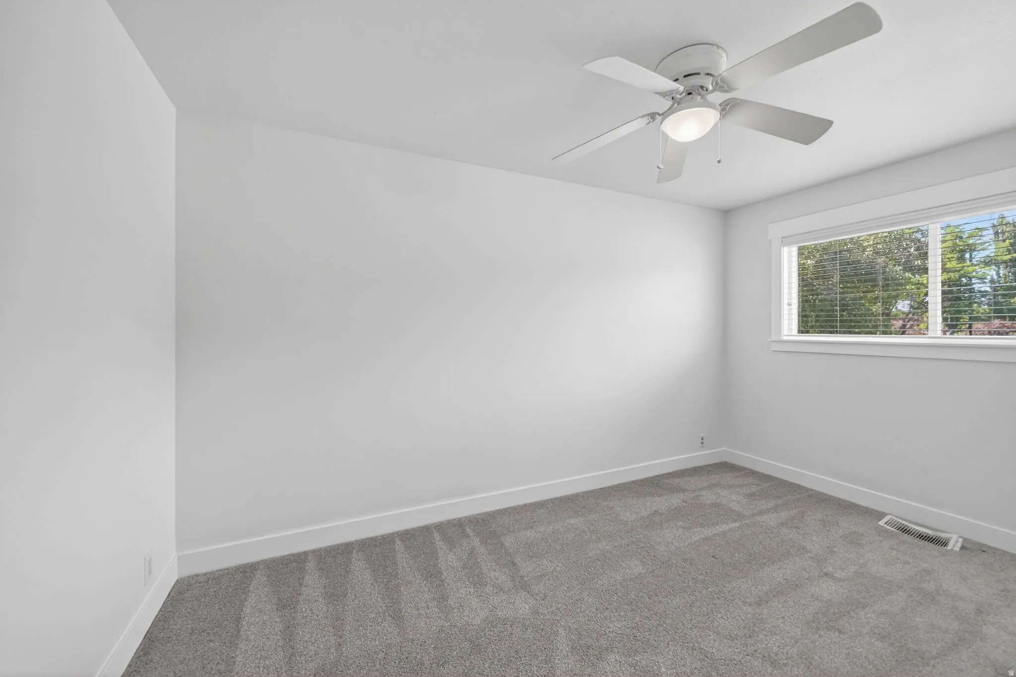 Bright room featuring a ceiling fan with integrated lighting, a large window with blinds, and neutral grey carpeting