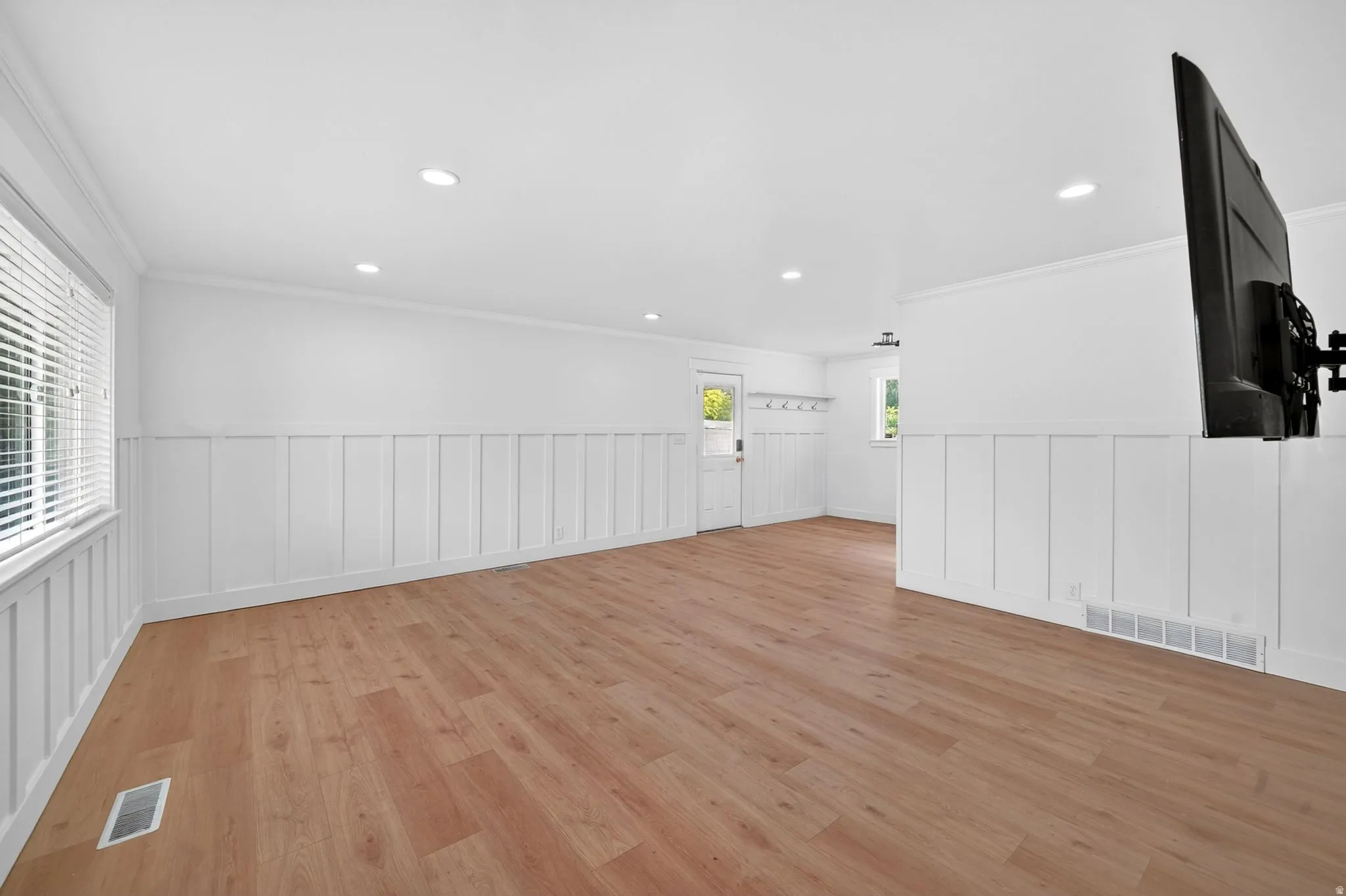 Spacious room featuring wood-finish flooring, white board and batten wall paneling, recessed lighting, and crown molding