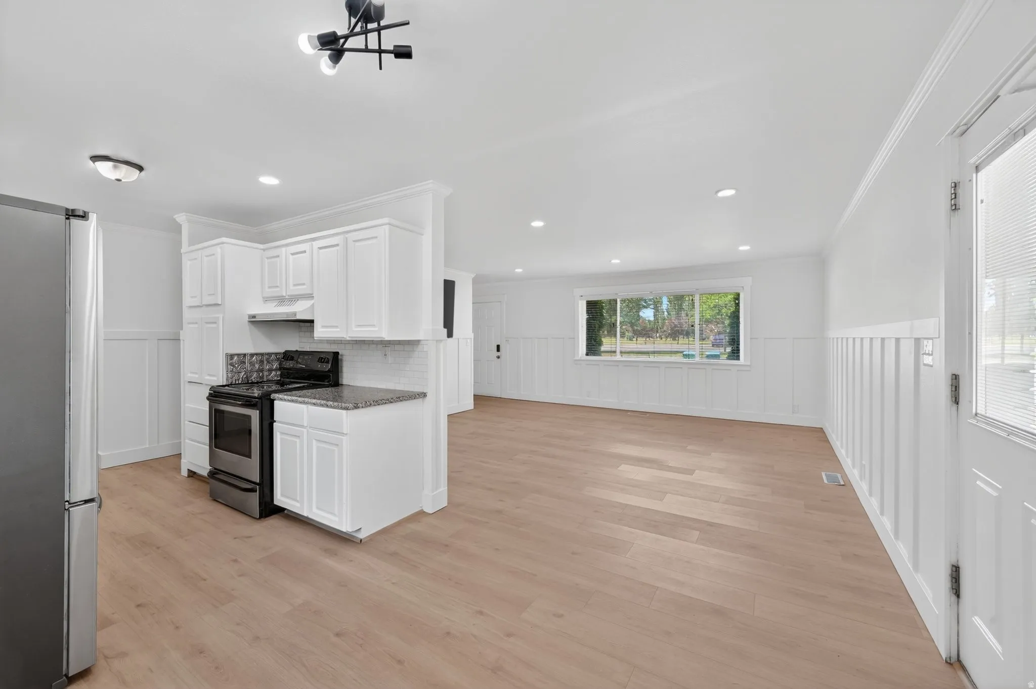 Bright kitchen area featuring white cabinetry, a tile backsplash, stainless steel appliances, granite-style countertops, and wood-finish flooring